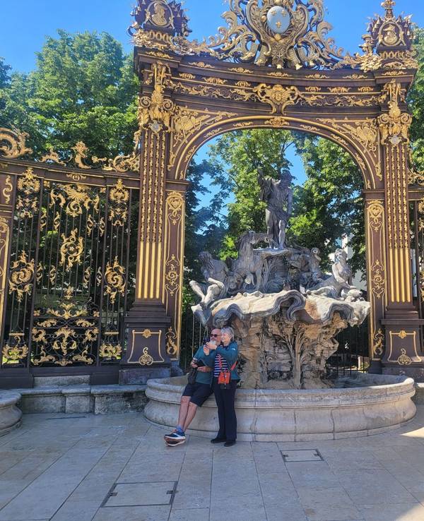 Zwei Menschen lehnen an einem Brunnen, der den Meeresgott Neptun zeigt und der von einem goldenen Bogen überspannt ist.