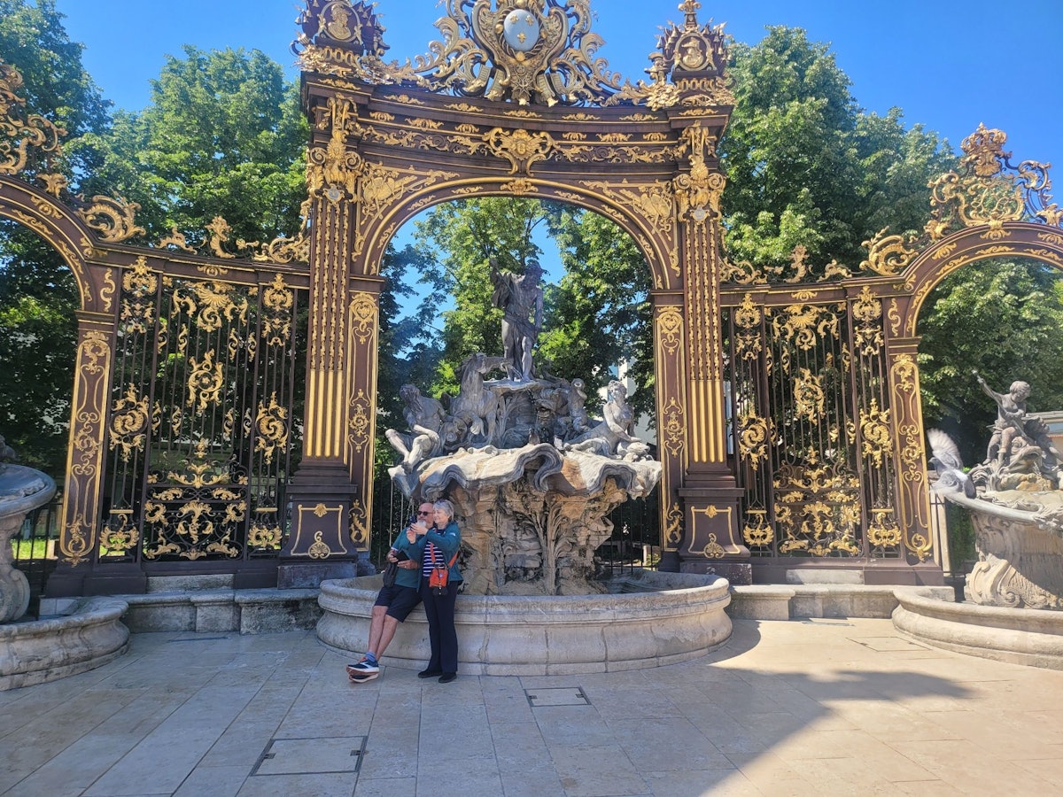 Zwei Menschen lehnen an einem Brunnen, der den Meeresgott Neptun zeigt und der von einem goldenen Bogen überspannt ist.