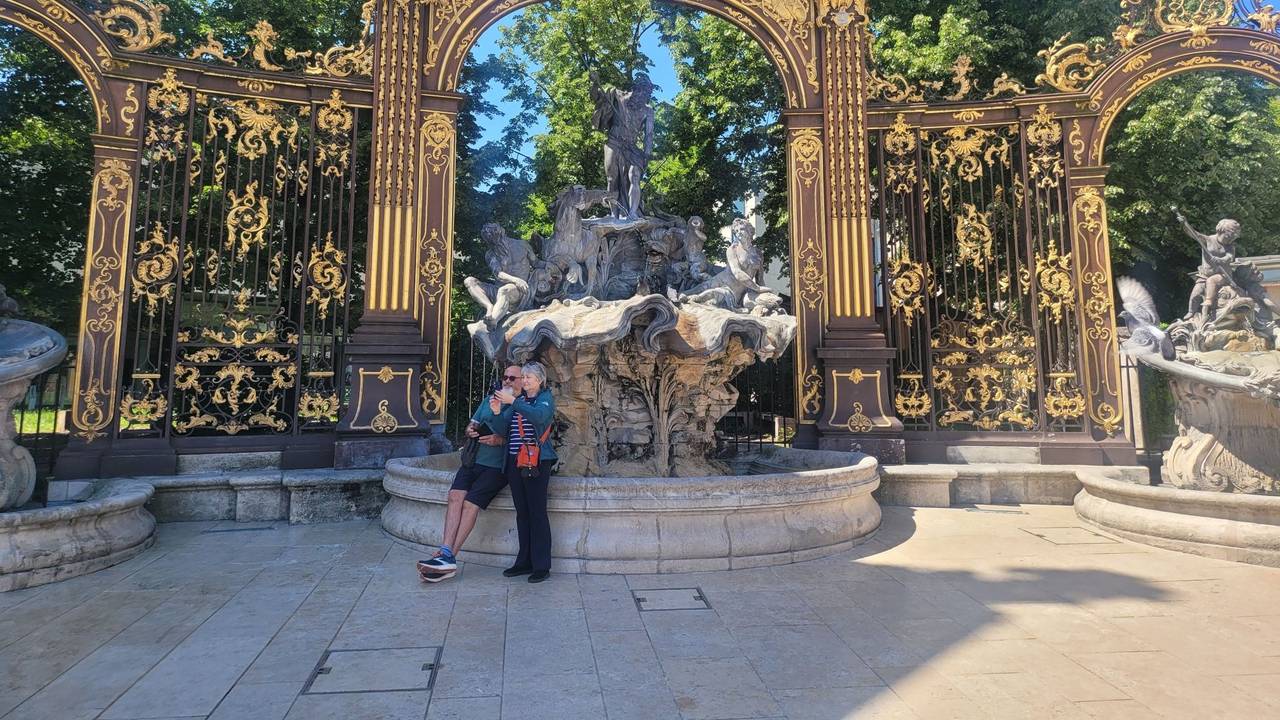 Zwei Menschen lehnen an einem Brunnen, der den Meeresgott Neptun zeigt und der von einem goldenen Bogen überspannt ist.