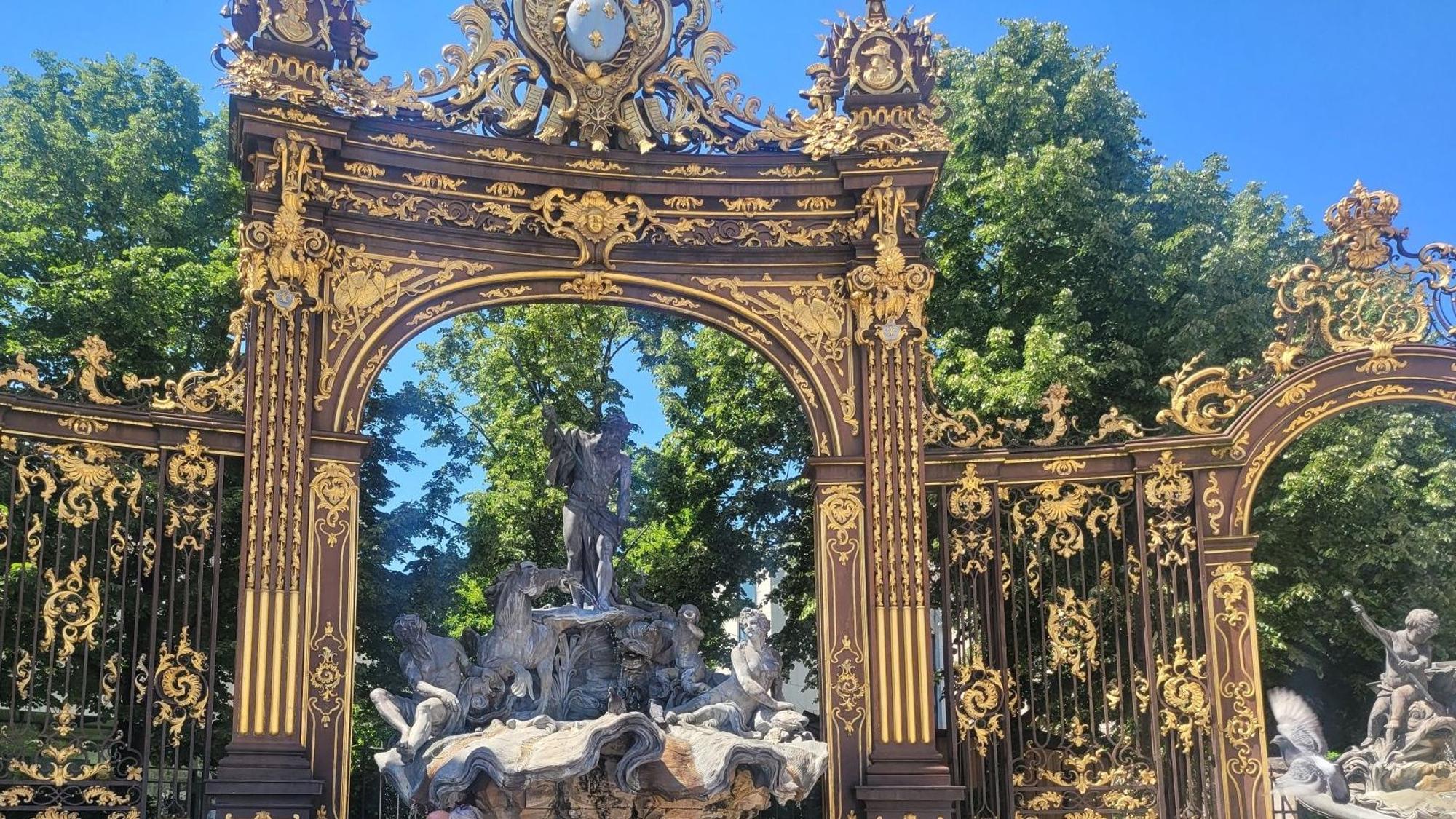 Zwei Menschen lehnen an einem Brunnen, der den Meeresgott Neptun zeigt und der von einem goldenen Bogen überspannt ist.