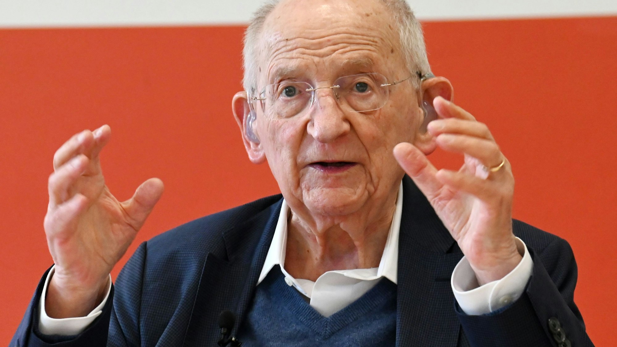 Ein alter Herr mit Hörgerät und weißem Haar gestikuliert und redet