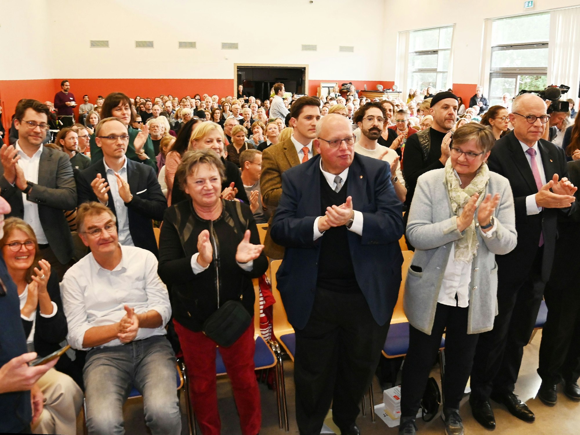 Menschen stehen in einem Saal und klatschen Beifall.