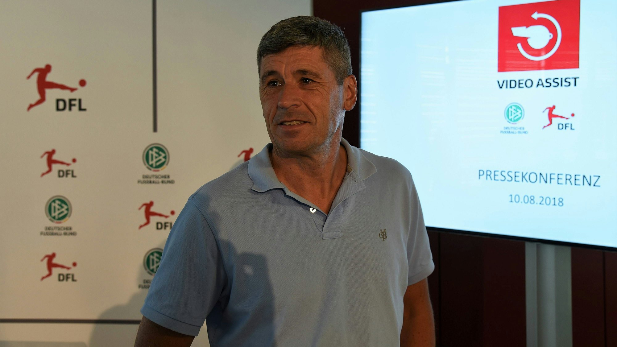 Dr. Markus Merk steht vor einem Fernseher mit dem Logo des Video-Assistenten.