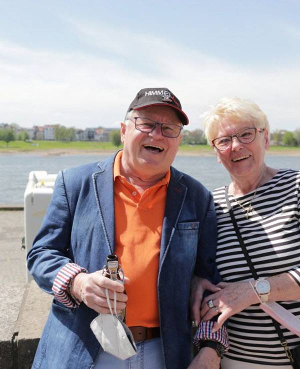 Ein Mann und eine Frau stehen eingehakt an einer Mauer am Rhein.