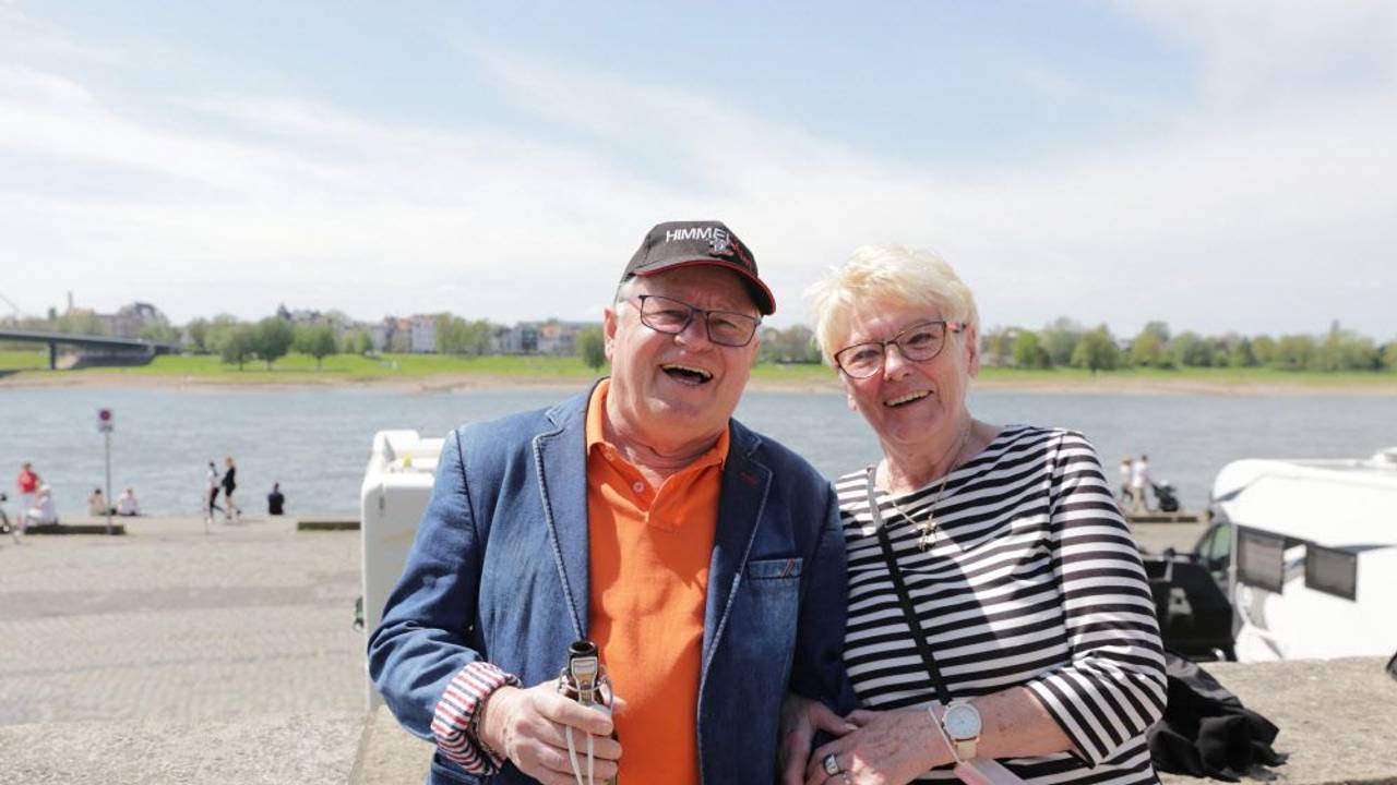 Ein Mann und eine Frau stehen eingehakt an einer Mauer am Rhein.