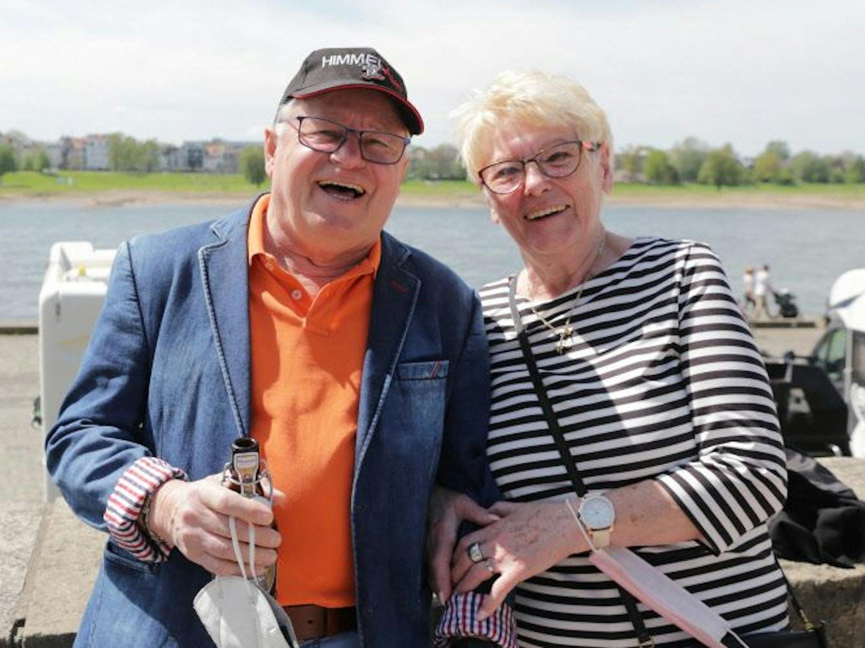 Ein Mann und eine Frau stehen eingehakt an einer Mauer am Rhein.