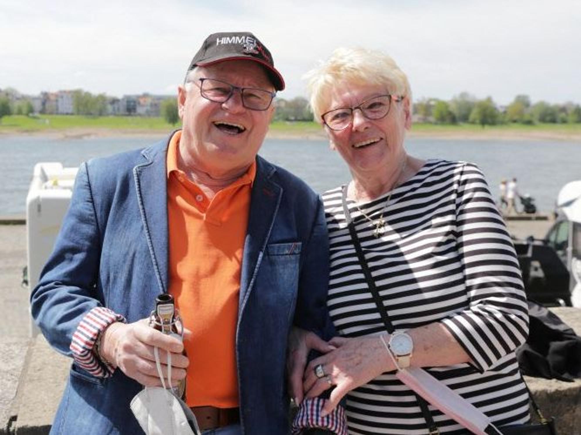 Ein Mann und eine Frau stehen eingehakt an einer Mauer am Rhein.