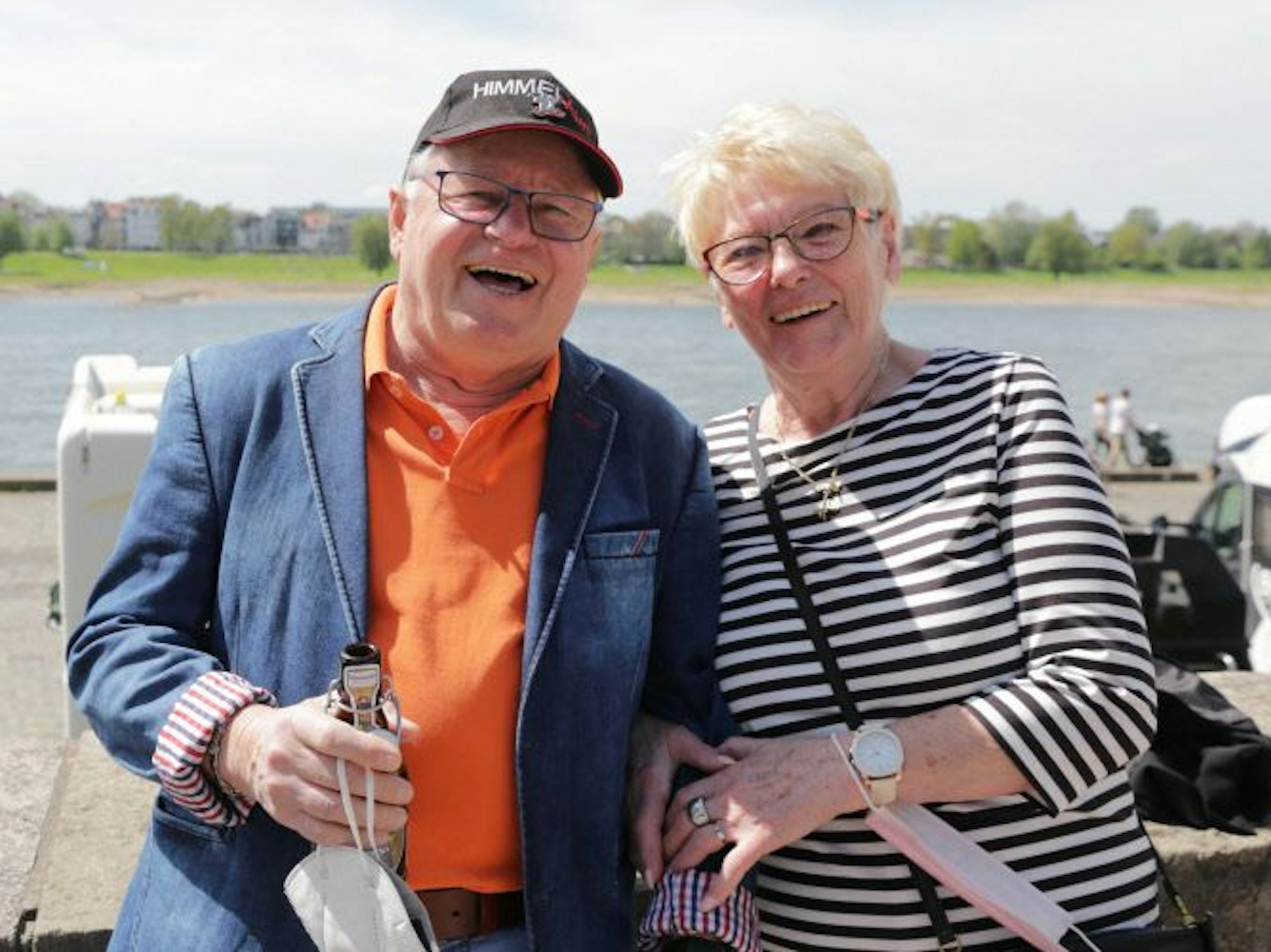 Ein Mann und eine Frau stehen eingehakt an einer Mauer am Rhein.