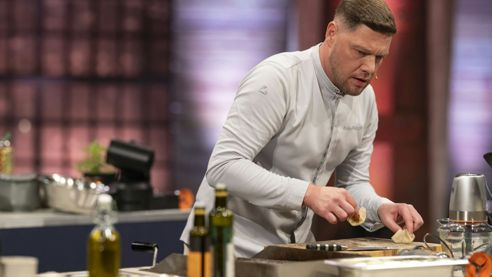 Ein Mann steht in einer Küche vor einem Schneidebrett.