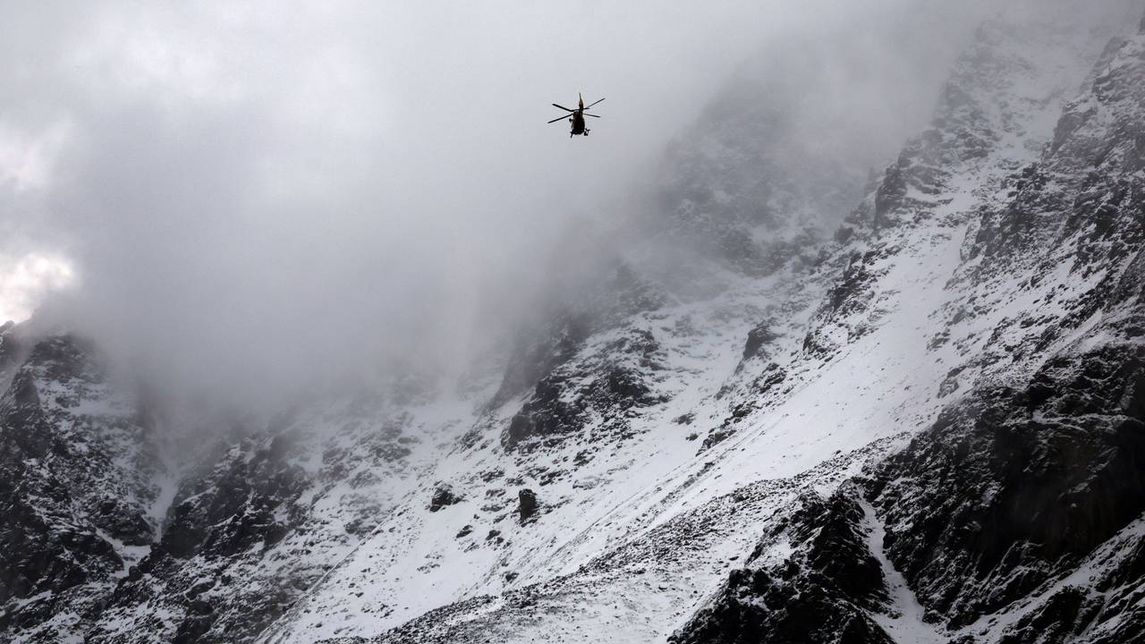 Ein Hubschrauber fliegt an schneebedeckten Berghängen vorbei.
