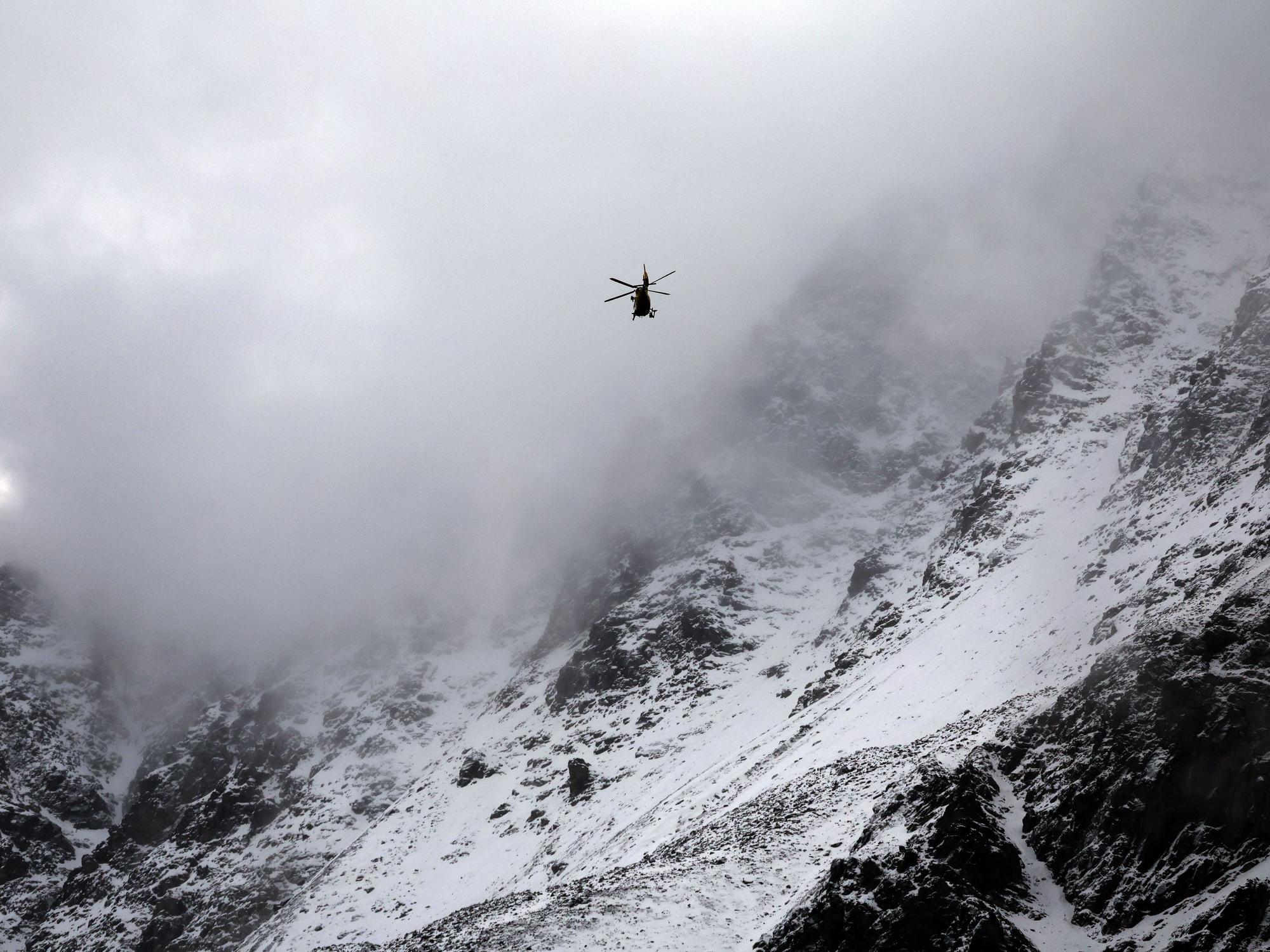 Ein Hubschrauber fliegt an schneebedeckten Berghängen vorbei.