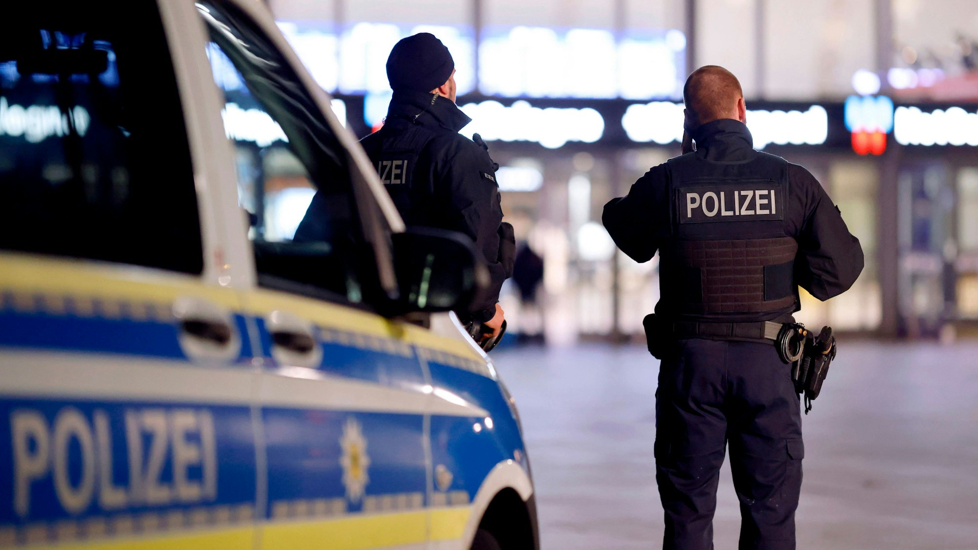 Zwei Polizisten und ein Polizeifahrzeug stehen am Kölner Hauptbahnhof.
