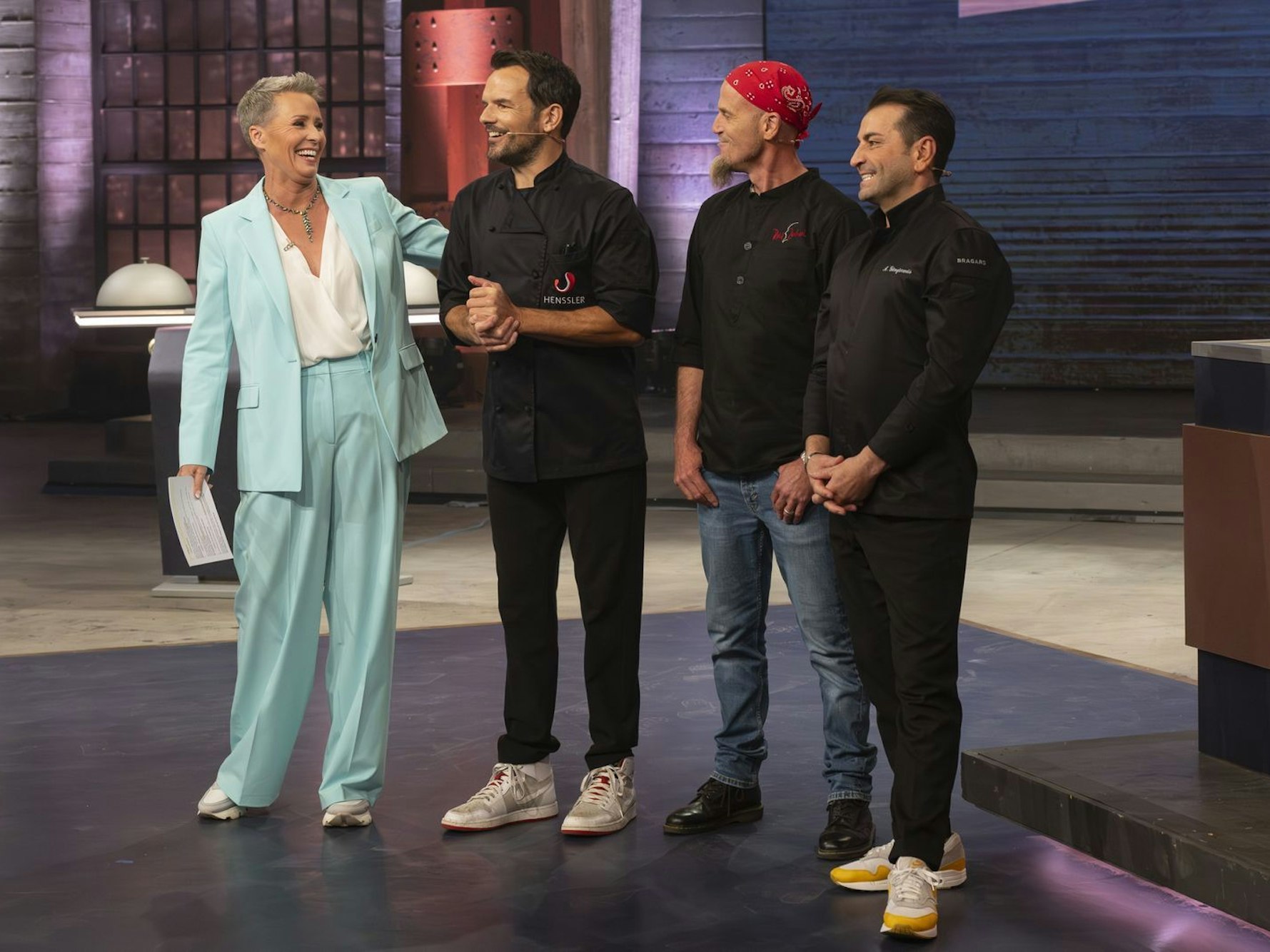 Eine Frau steht neben drei Männern in einem TV-Studio.