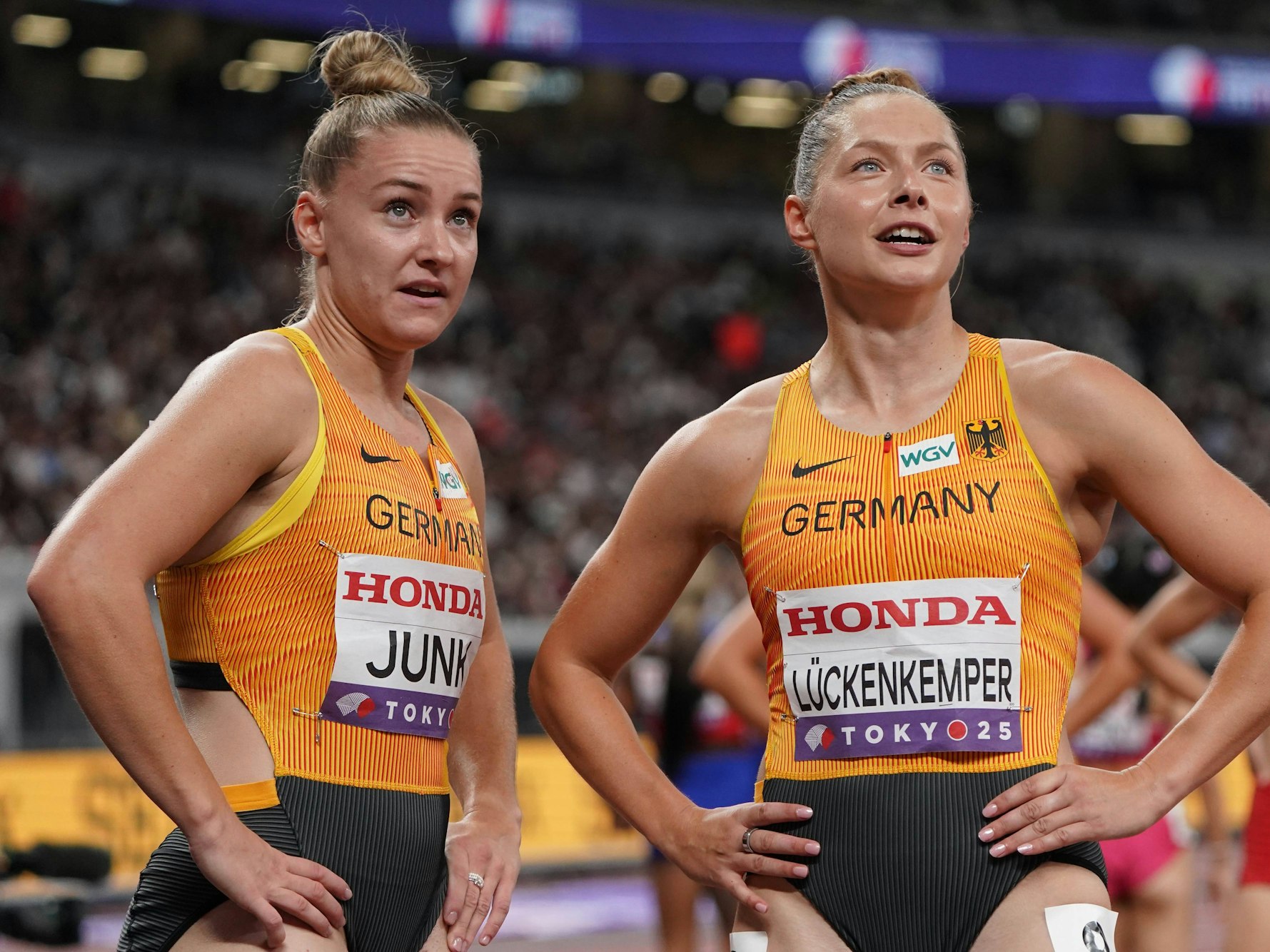 Sophia Junk und Gina Lückenkemper schauen kurz nach einem Wettkampf nach oben auf den Bildschirm im Stadion.