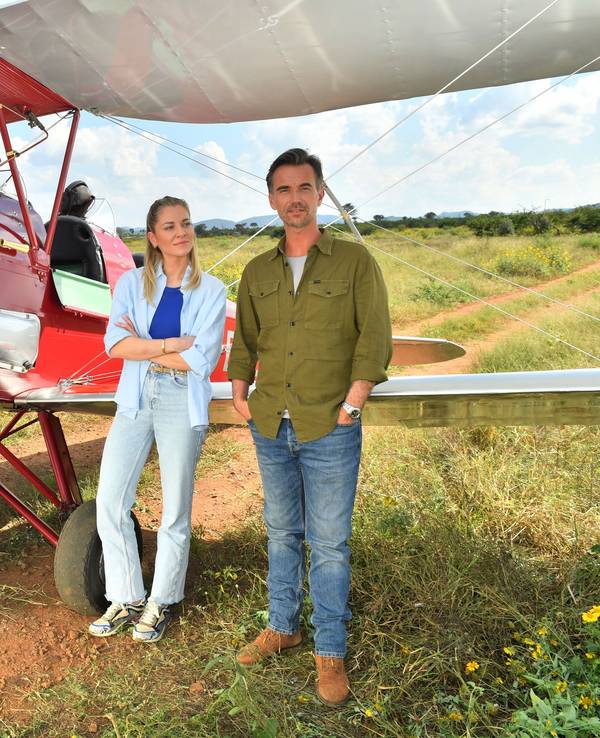 Szene aus dem ZDF-Traumschiff: Sophia Berg (Valentina Pahde) und Max Parger (Florian Silbereisen) stehen vor einem roten Propeller-Flugzeug in der afrikanischen Savanne
