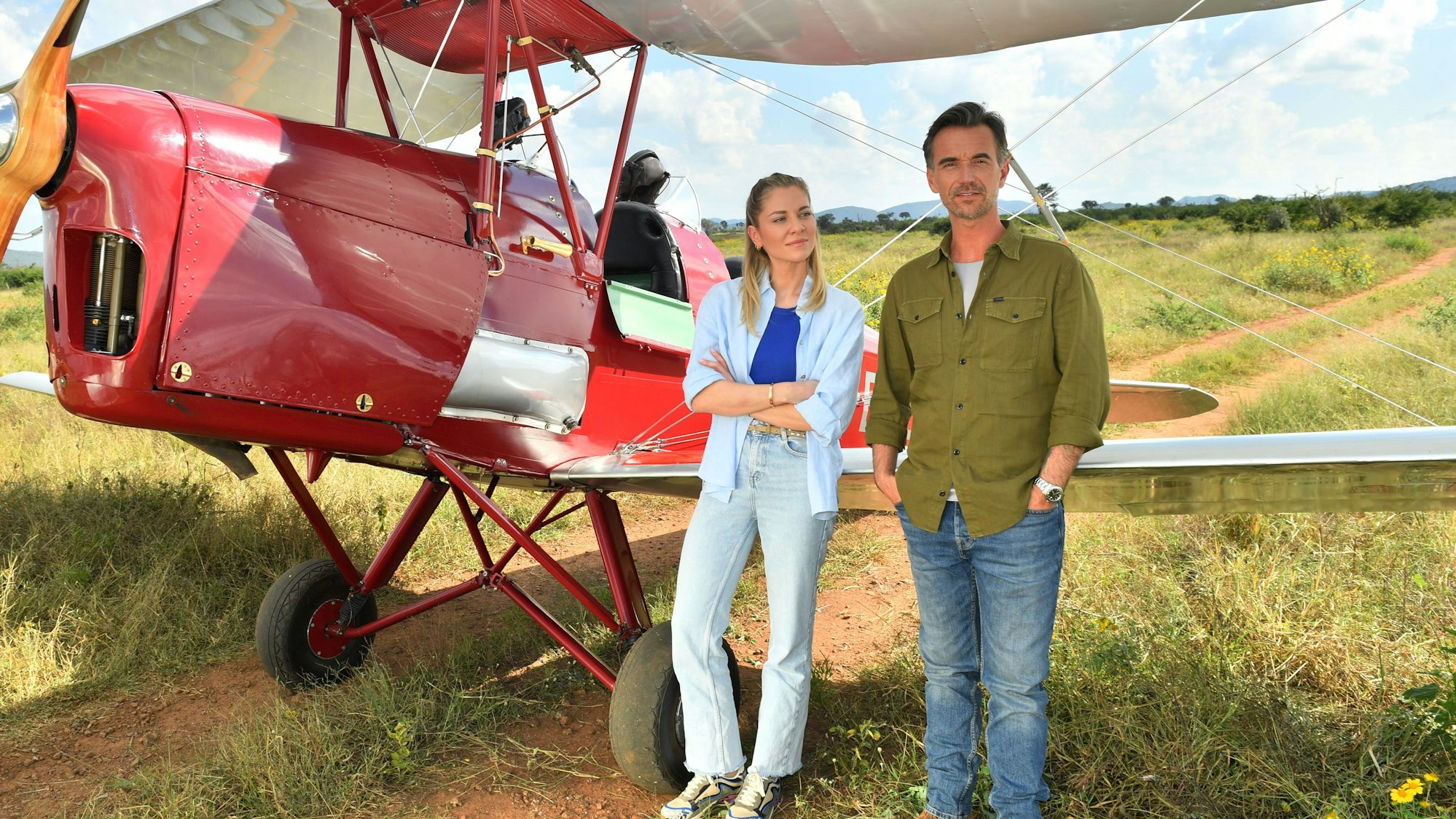 Szene aus dem ZDF-Traumschiff: Sophia Berg (Valentina Pahde) und Max Parger (Florian Silbereisen) stehen vor einem roten Propeller-Flugzeug in der afrikanischen Savanne