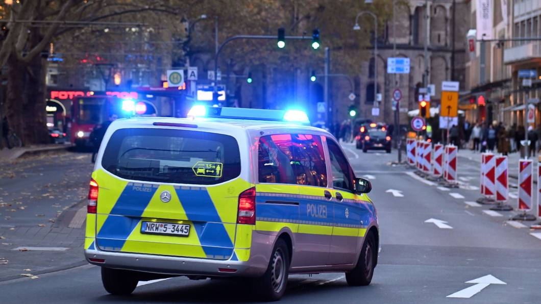 Ein Polizeiauto rast mit Blaulicht am Kölner Neumarkt an Passanten vorbei.