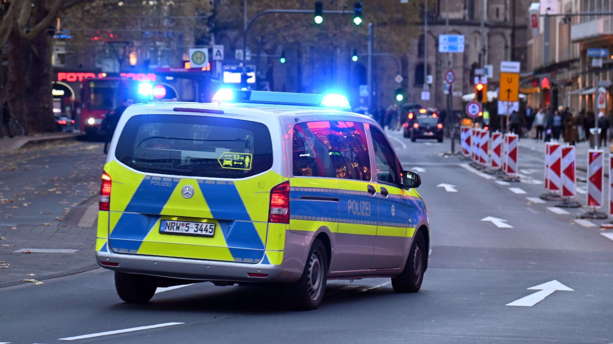 Ein Polizeiauto rast mit Blaulicht am Kölner Neumarkt an Passanten vorbei.