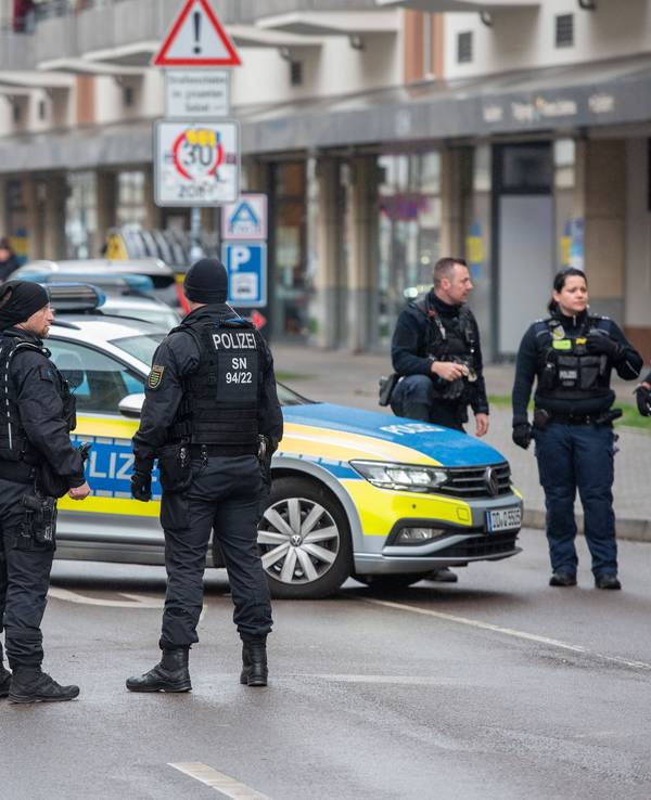 Polizistinnen und Polizisten stehen neben einem Polizeiauto auf der Straße.