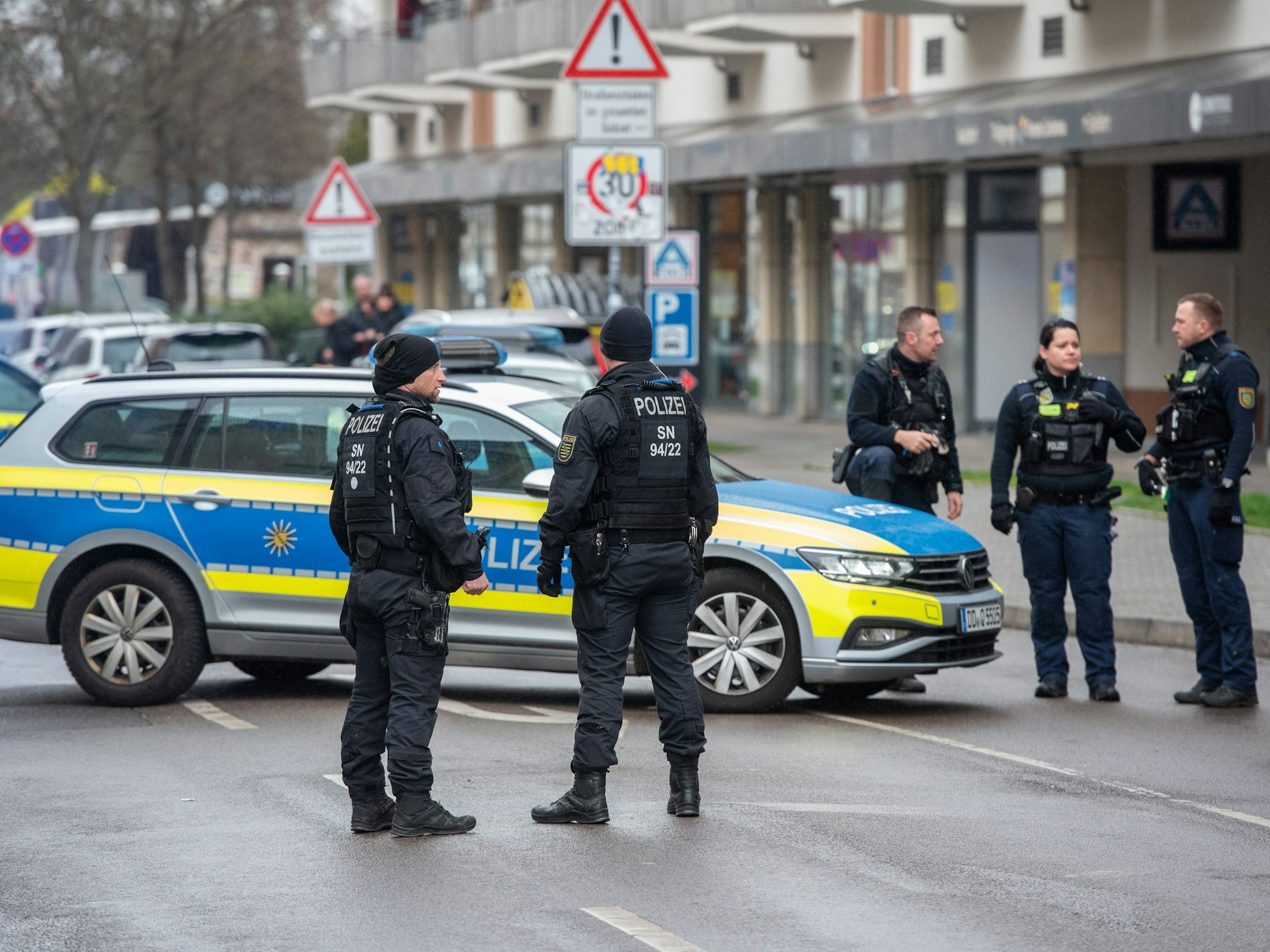 Polizistinnen und Polizisten stehen neben einem Polizeiauto auf der Straße.