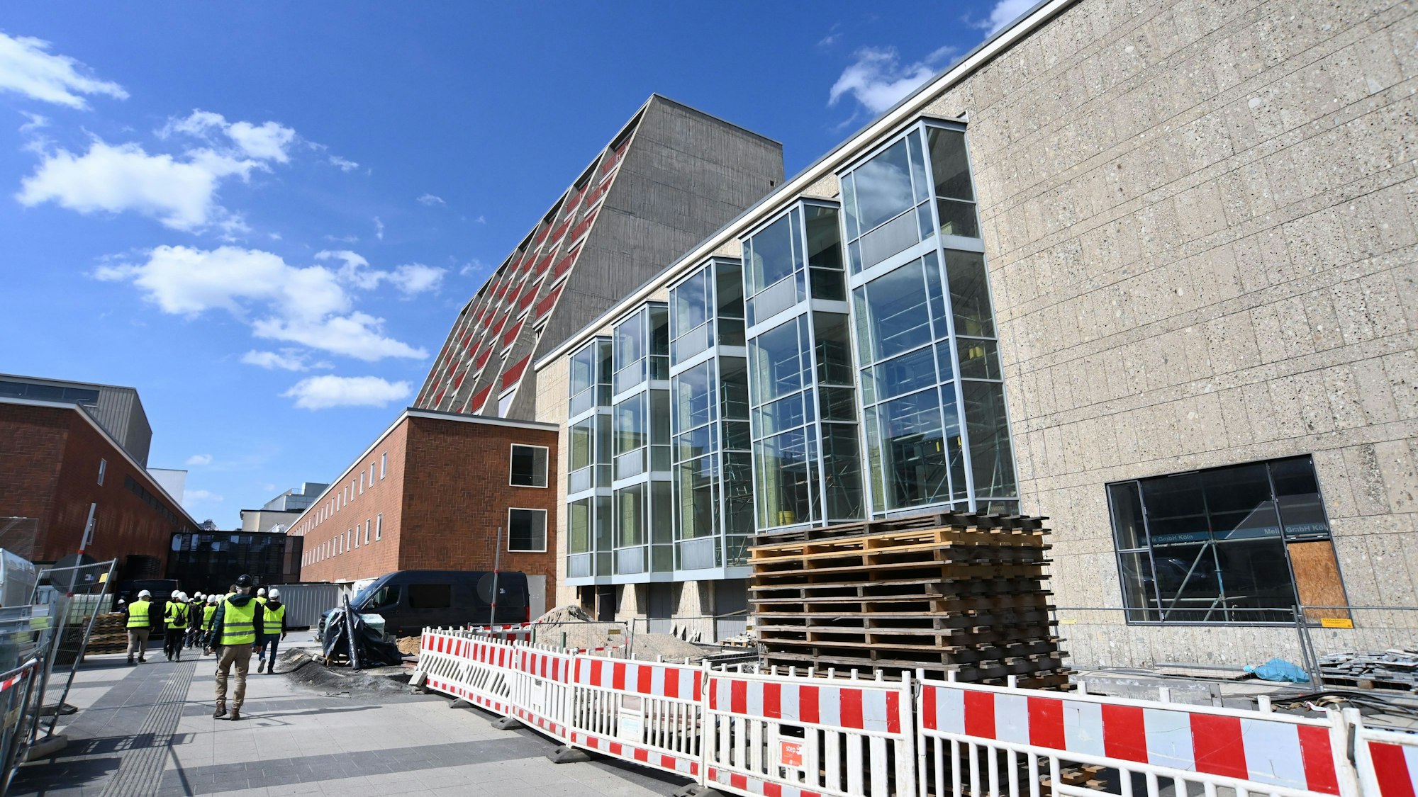 Seitlich an einem Gebäude steht ein Bauzaun, dahinter sind Baumaterialien gelagert.