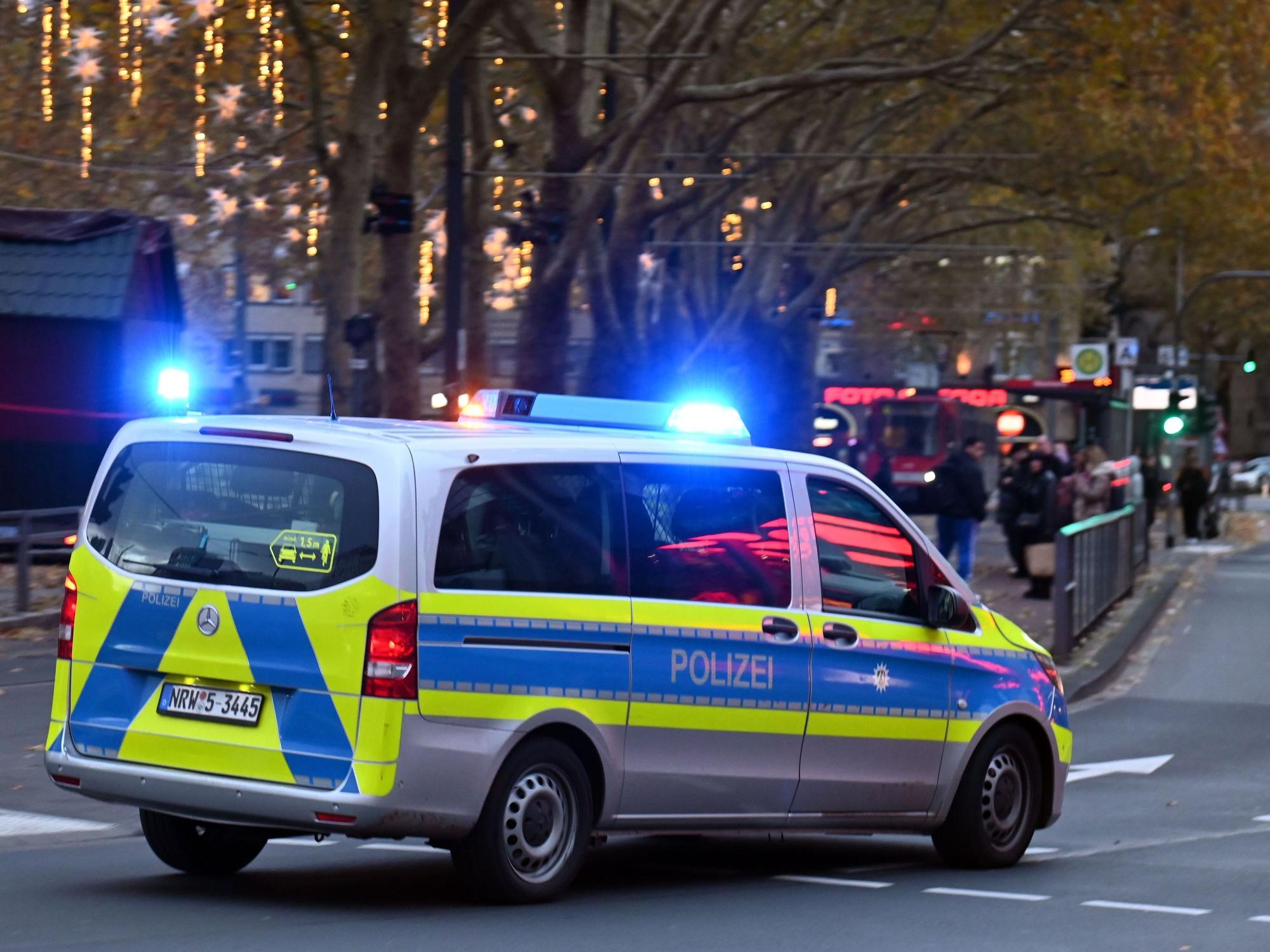 Ein Polizeiauto rast mit Blaulicht an Passanten vorbei.