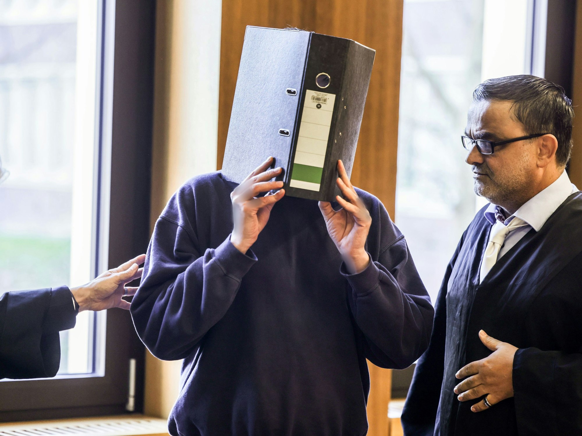 Der Angeklagte Krankenpfleger (M) steht im November 2025 mit einem Aktenordner vor dem Gesicht neben seinem Anwalt Volker Breyer (r) im Gerichtssaal des Aachener Landgerichts.