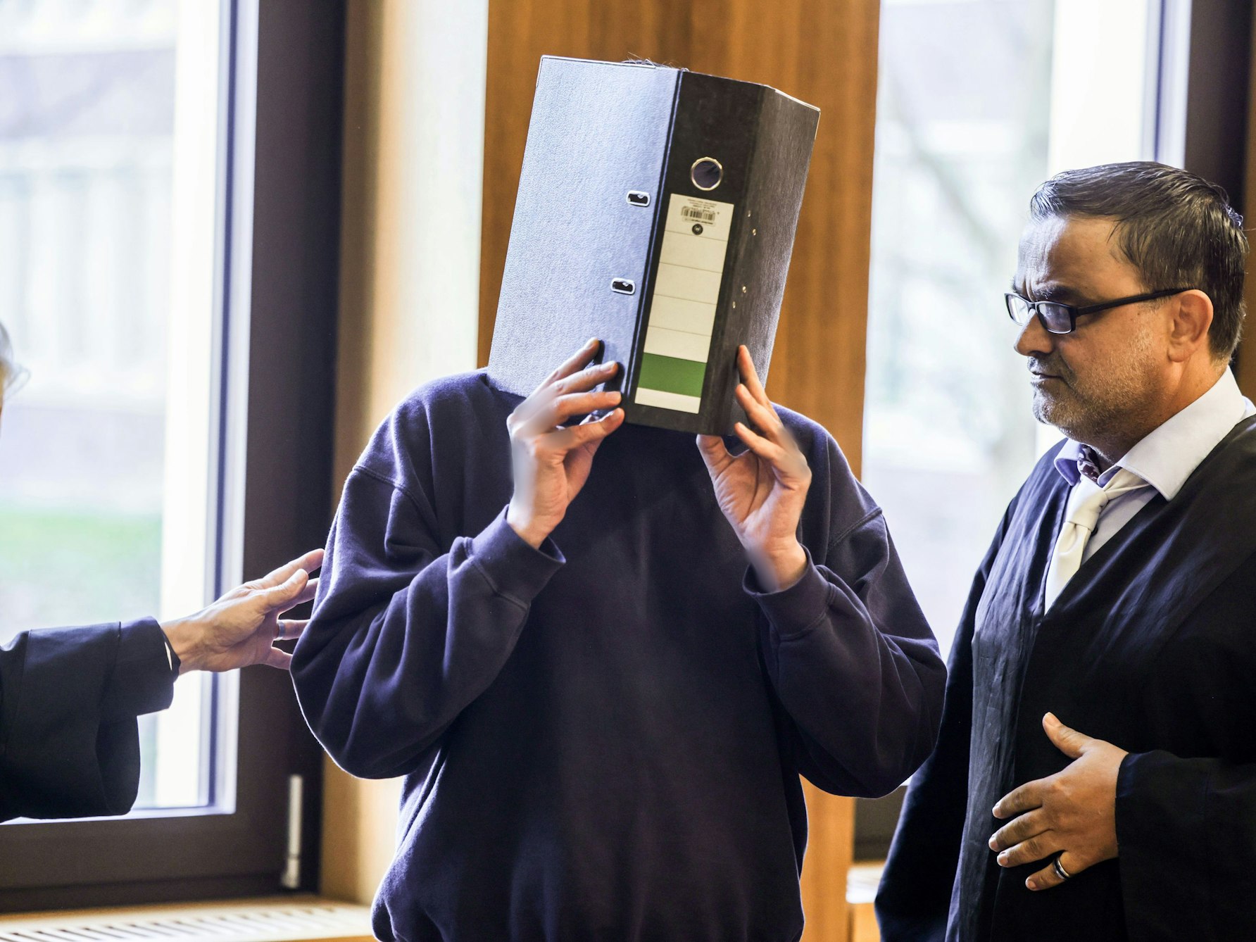 Der Angeklagte Krankenpfleger (M) steht mit einem Aktenordner vor dem Gesicht neben seinem Anwalt Volker Breyer (r) im Gerichtssaal.