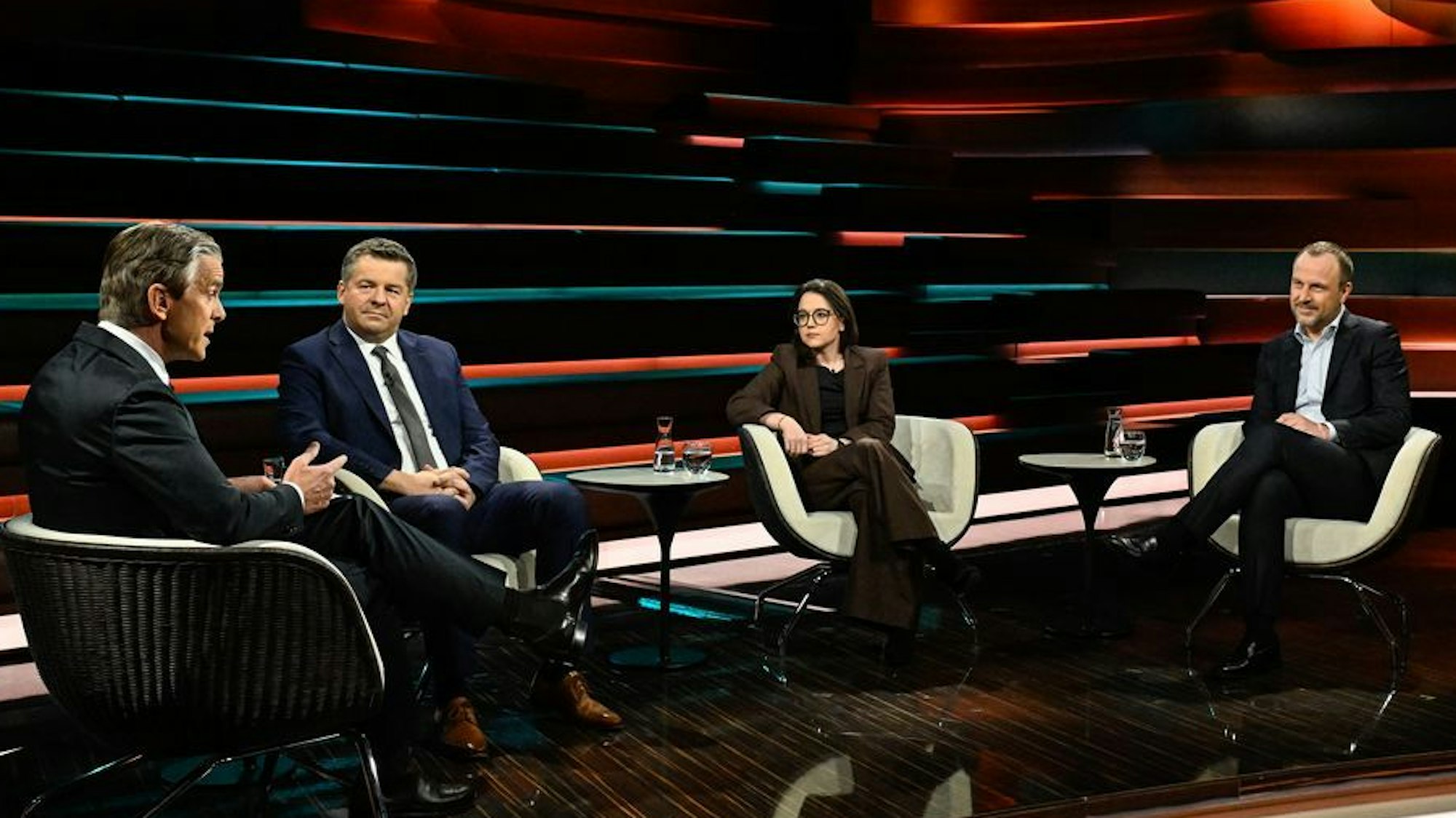 Drei Männer und eine Frau sitzen in einem TV-Studio, einer der Männer gestikuliert, die anderen Personen schauen zu ihm hin.