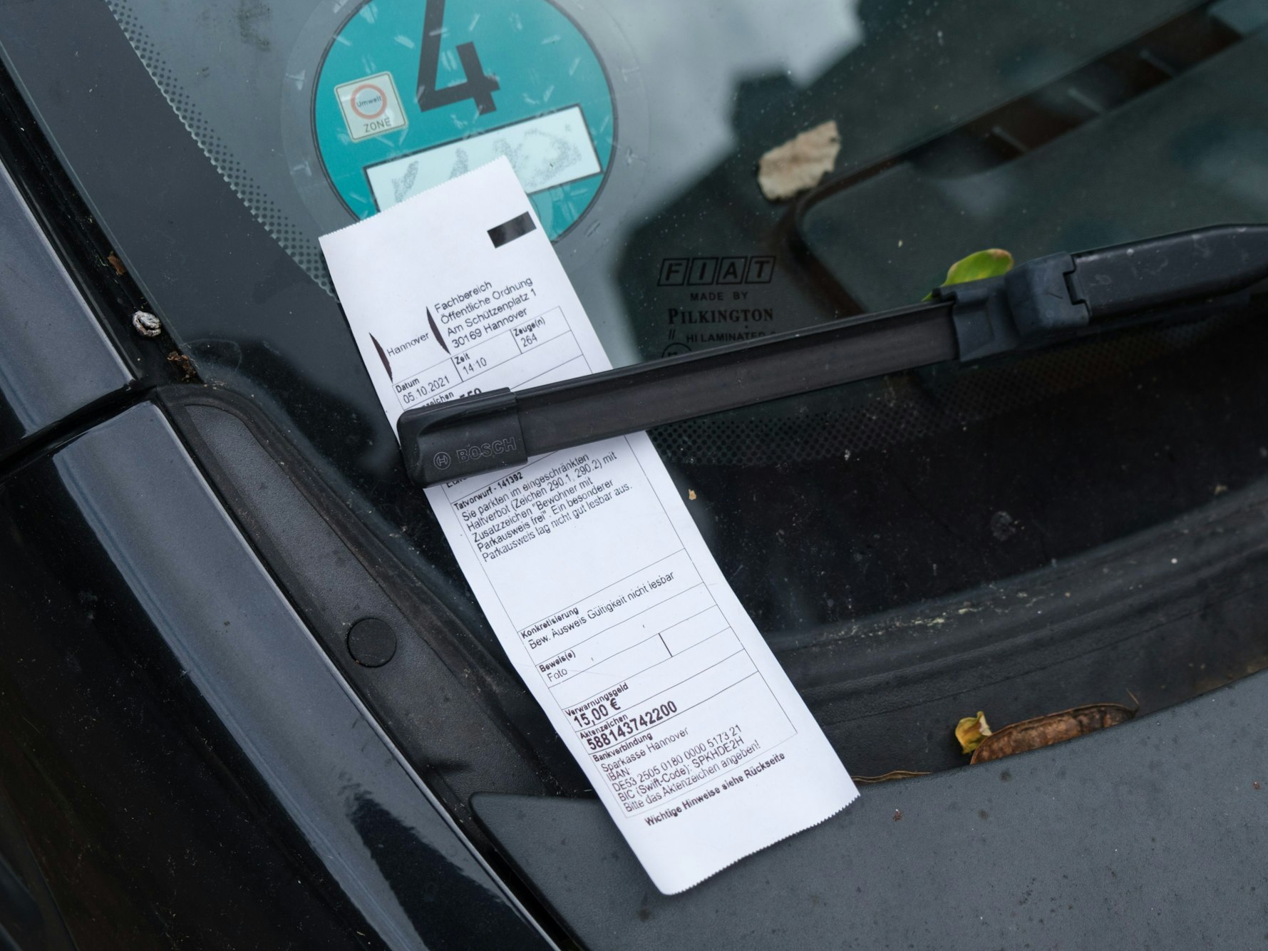 Ein Strafzettel klemmt hinter einem Scheibenwischer.