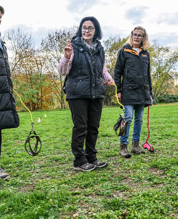 Hundetrainerin Barbara Gerlinger (Mitte) hält eine Hundeleine in der Hand und erklärt Teilnehmern des Kurses das Hobby-Dogging. Beim Hobby-Dogging tut man Dinge, die man mit einem Hund tun würde - nur eben ohne Tier.