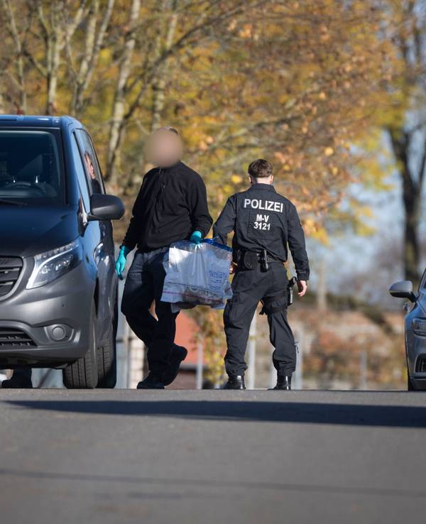 Ein Ermitter läuft mit Plastiktüten, in der sich Sportschuhe befinden, bei einer Hausdurchsuchung in Reimershagen über die Straße