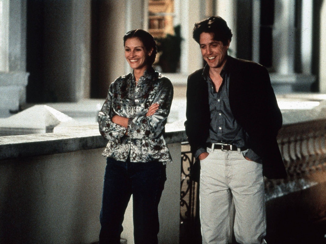 Ein Mann und eine Frau gehen lachend nebeneinander eine Straße herunter an altehrwürdigen Häusern vorbei.