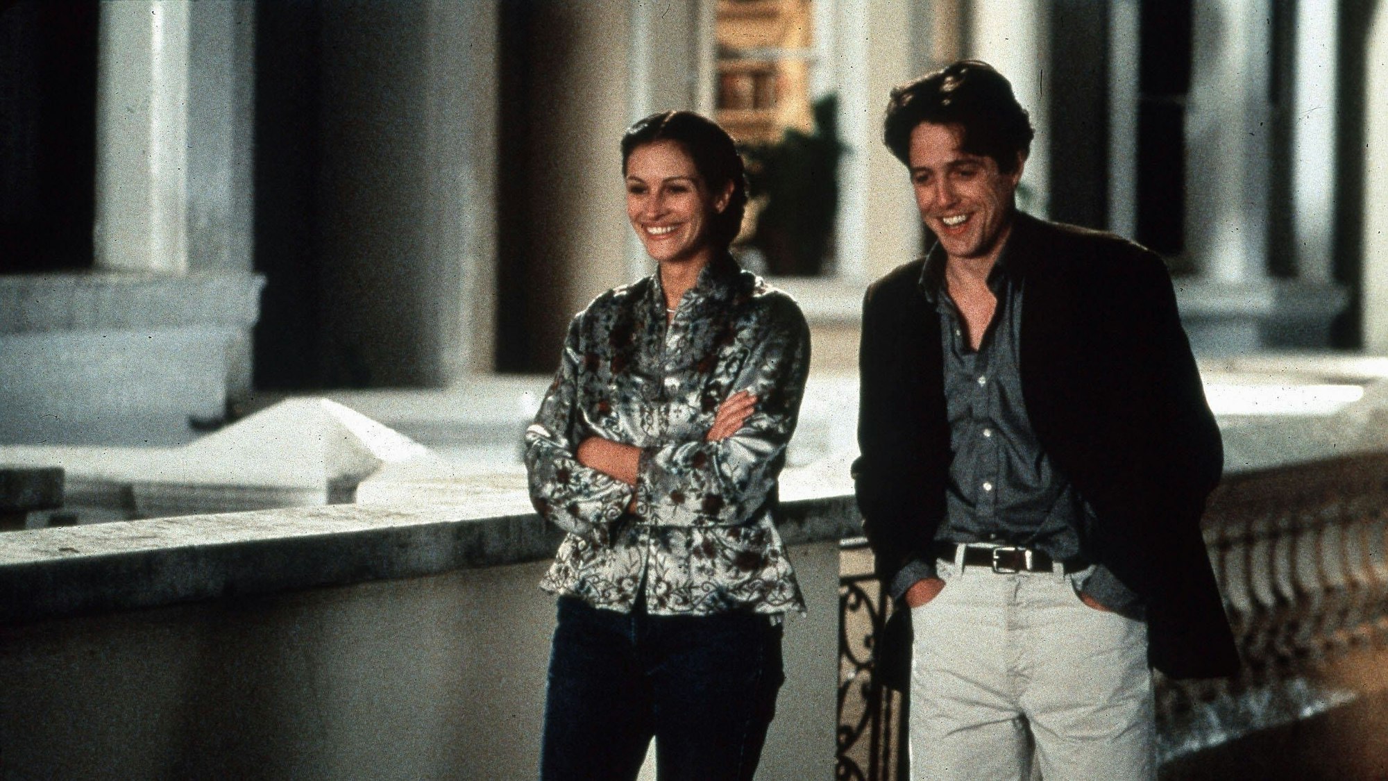 Ein Mann und eine Frau gehen lachend nebeneinander eine Straße herunter an altehrwürdigen Häusern vorbei.