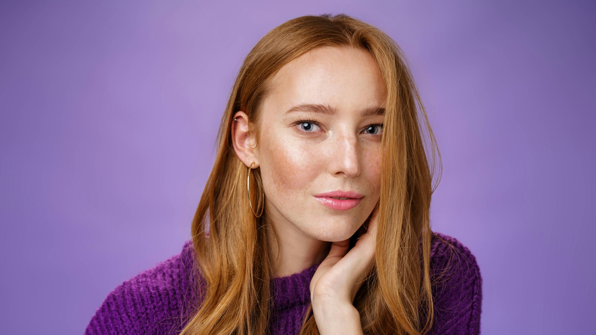 Eine Frau mit langen roten Haaren blickt in die Kamera. Sie trägt einen lila Pullover.