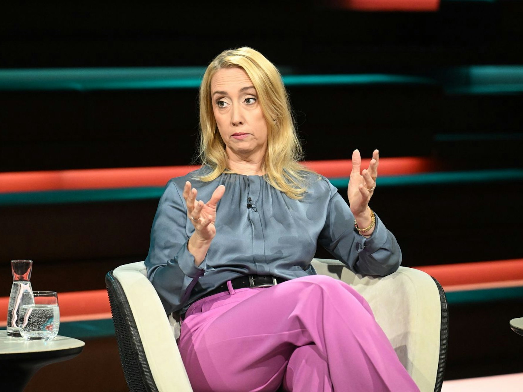 Eine Frau sitzt in einem TV-Studio und gestikuliert.