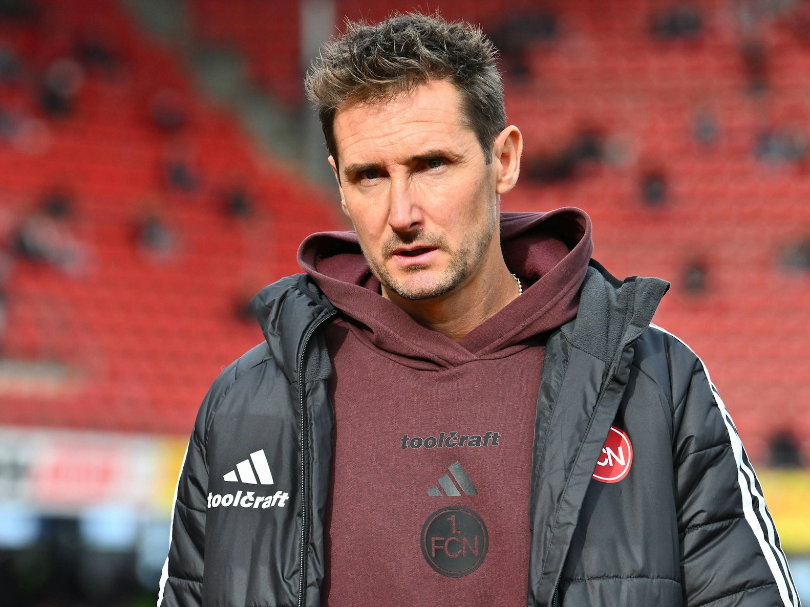 Miroslav Klose steht mit Jacke im Stadion.