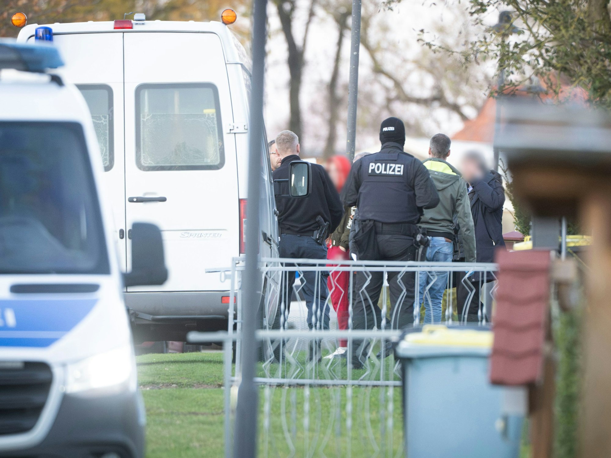 Eine Frau verlässt in Begleitung von Polizeibeamten ihr Wohnhaus.