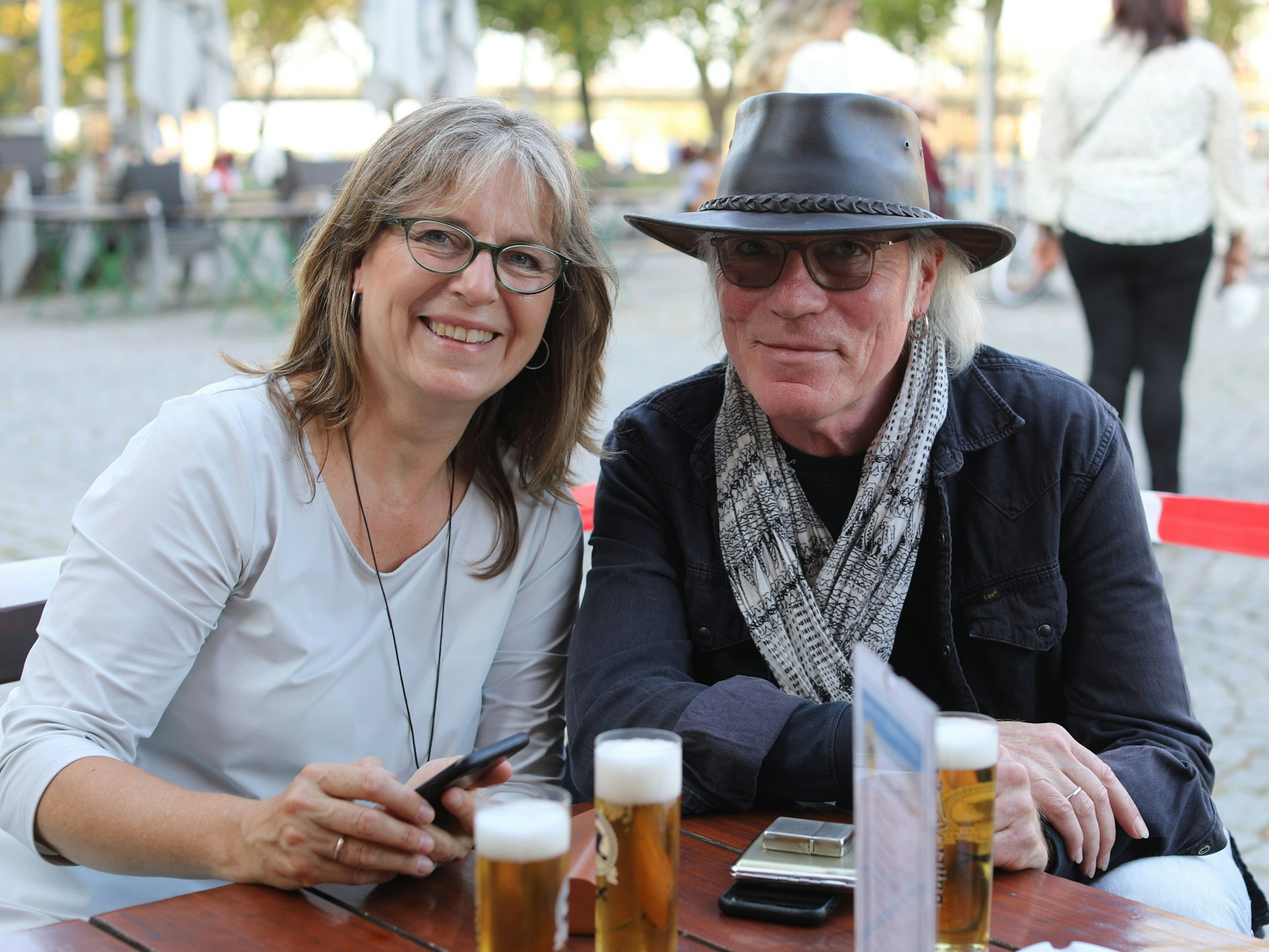Ein Mann und eine Frau sitzen draußen an einem Tisch, vor sich ein Glas Bier.