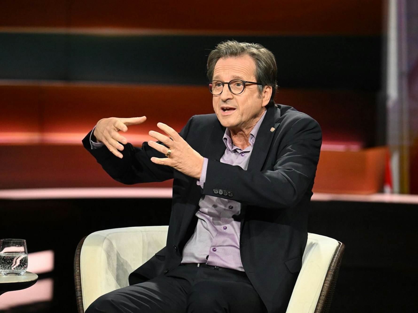 Ein Mann sitzt in einem TV-Studio und gestikuliert.