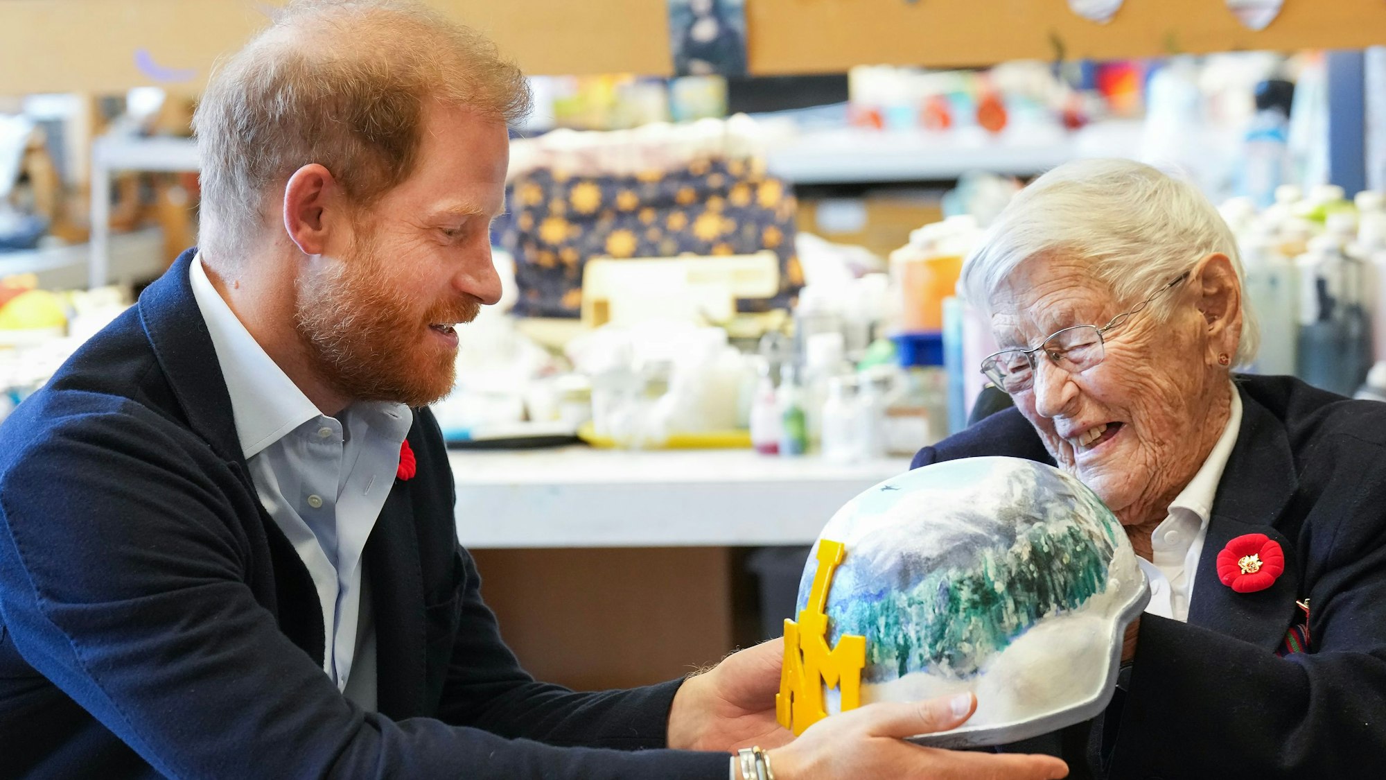 Prinz Harry erhält einen bemalten Armeehelm von der 101-jährigen Kriegsveteranin Brenda Reid.