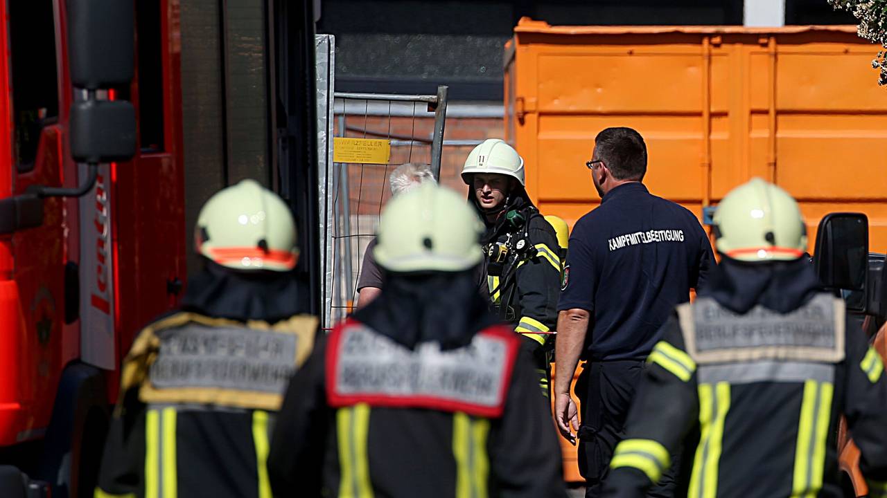 Feuwerwehrleute und Mitarbeiter des Kampfmittelräumdienstes gehen zu einem Schulhof.