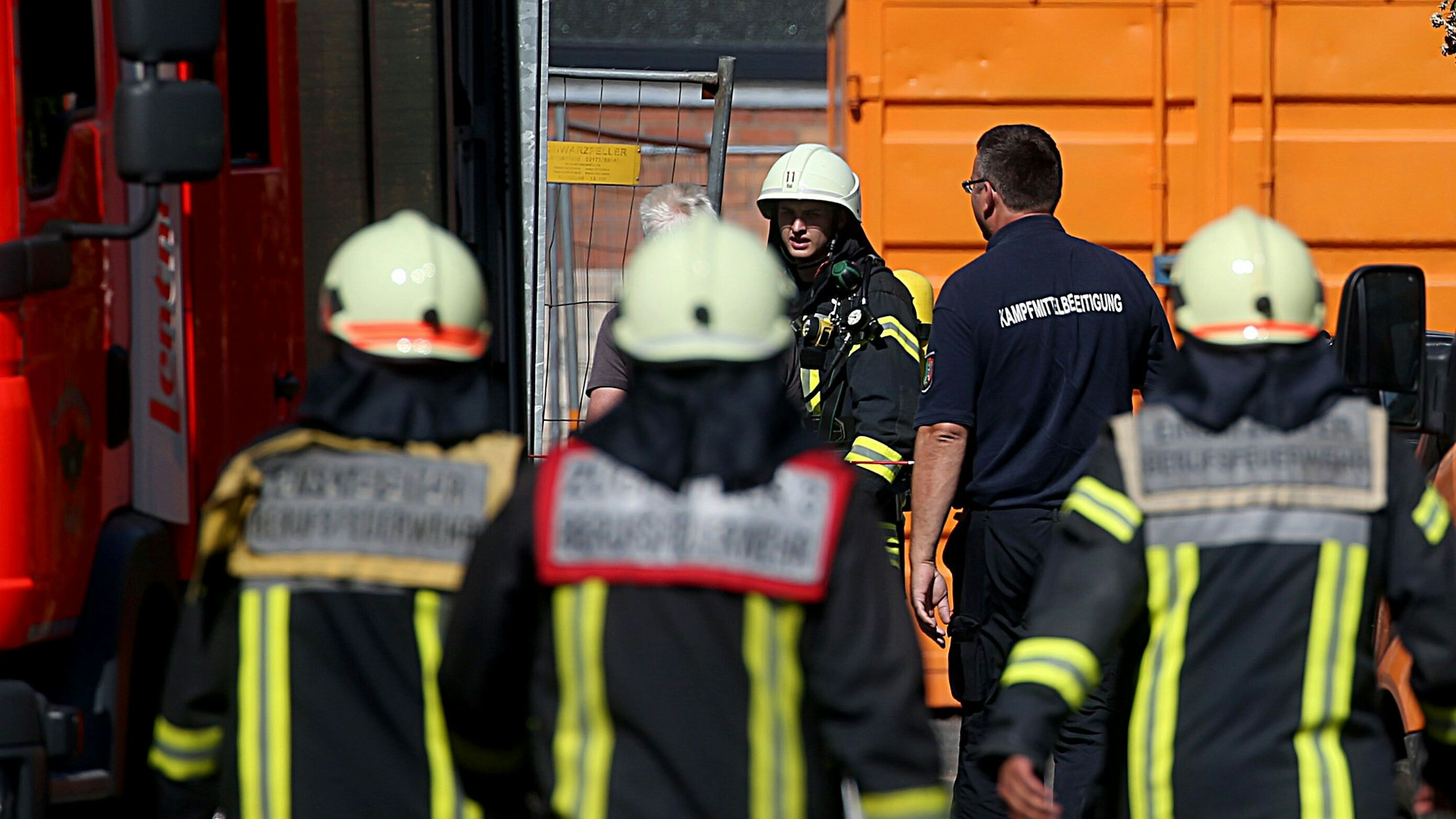 Feuwerwehrleute und Mitarbeiter des Kampfmittelräumdienstes gehen zu einem Schulhof.