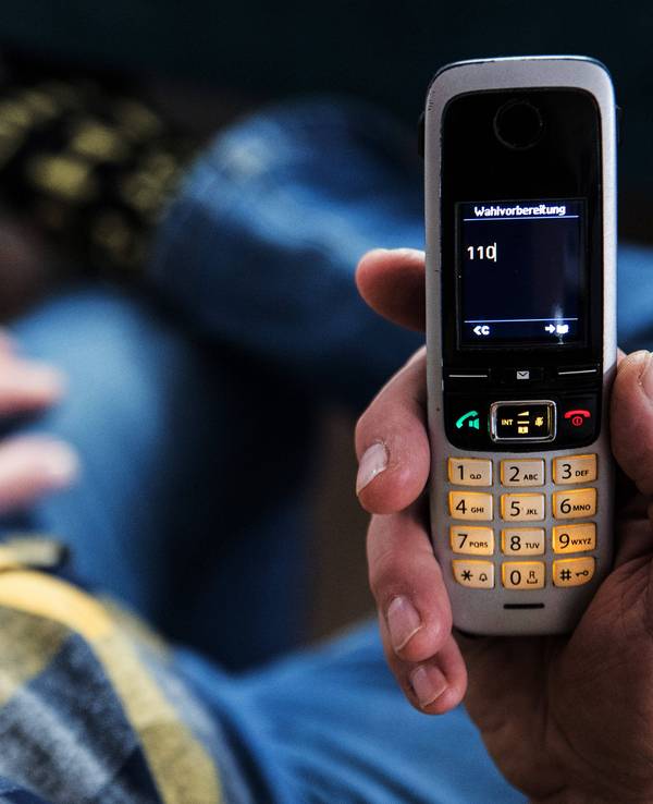 Ein älterer Menschen sitzt in seiner Wohnung und hält ein Mobiltelefon in der Hand auf dem Display des Telefons ist die 110 zu lesen.