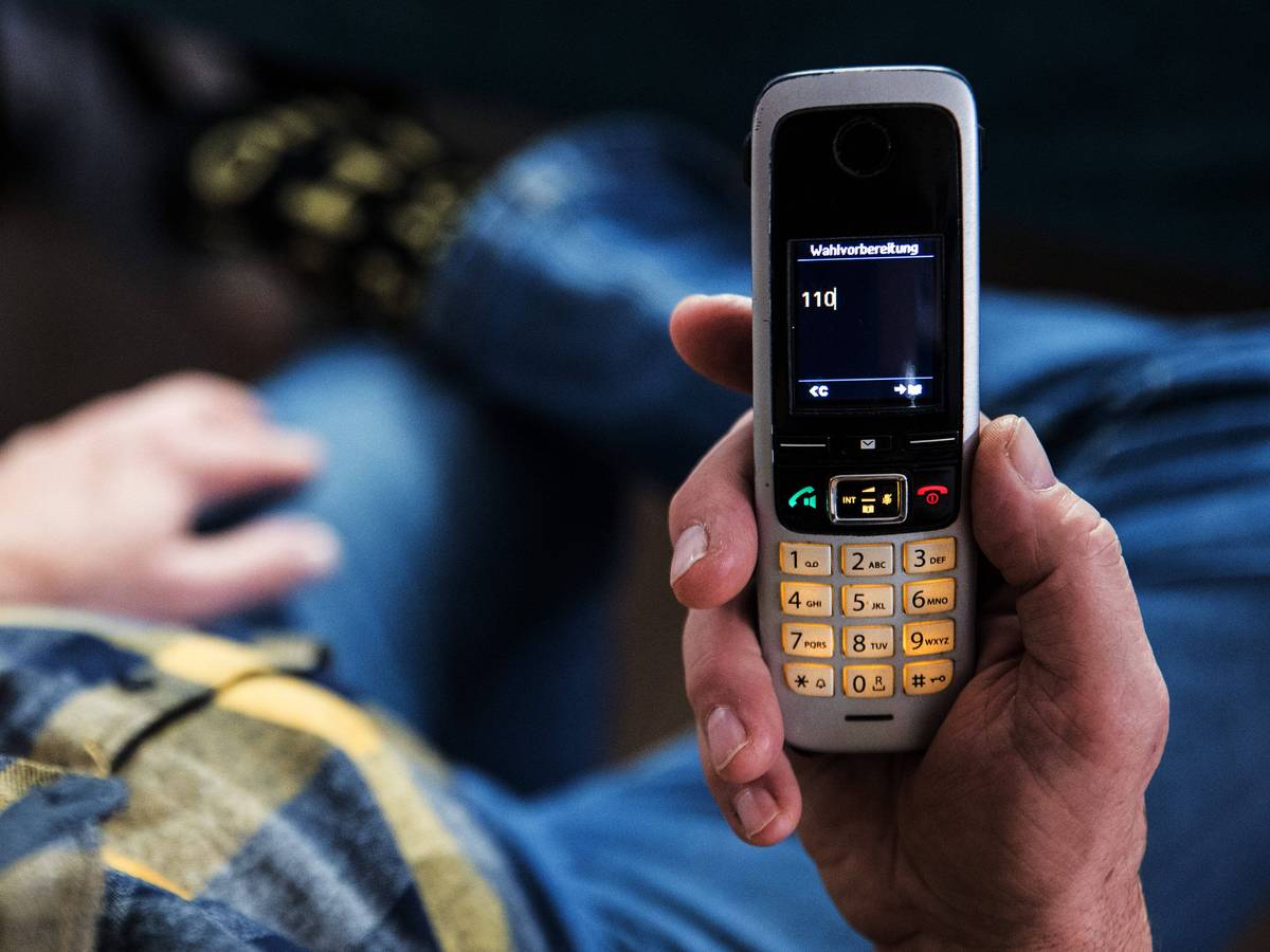 Ein älterer Menschen sitzt in seiner Wohnung und hält ein Mobiltelefon in der Hand auf dem Display des Telefons ist die 110 zu lesen.