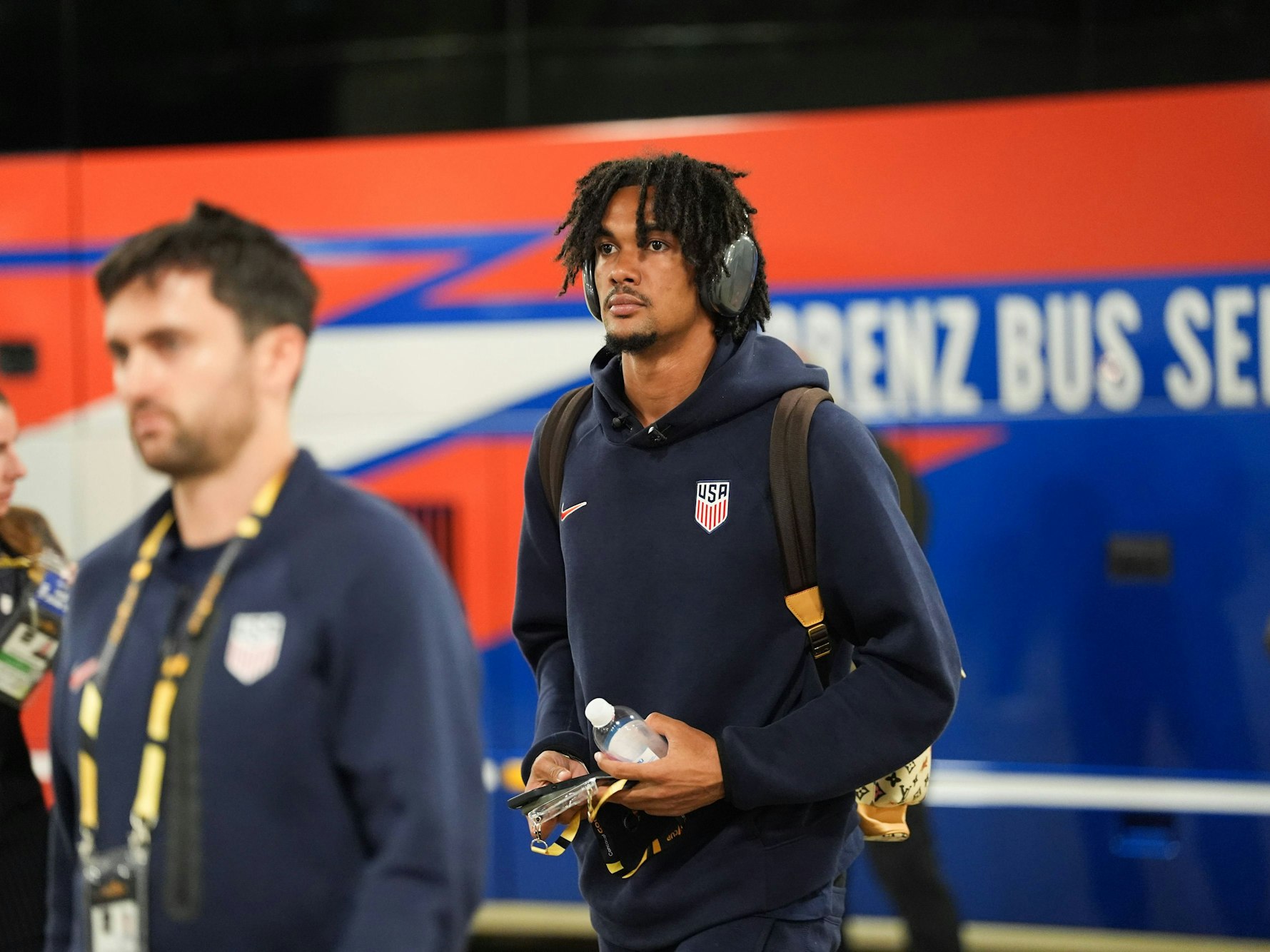 Damion Downs hat Kopfhörer an und läuft mit einem Rucksack und einer Flasche in der Hand durch die Katakomben eines Stadions.