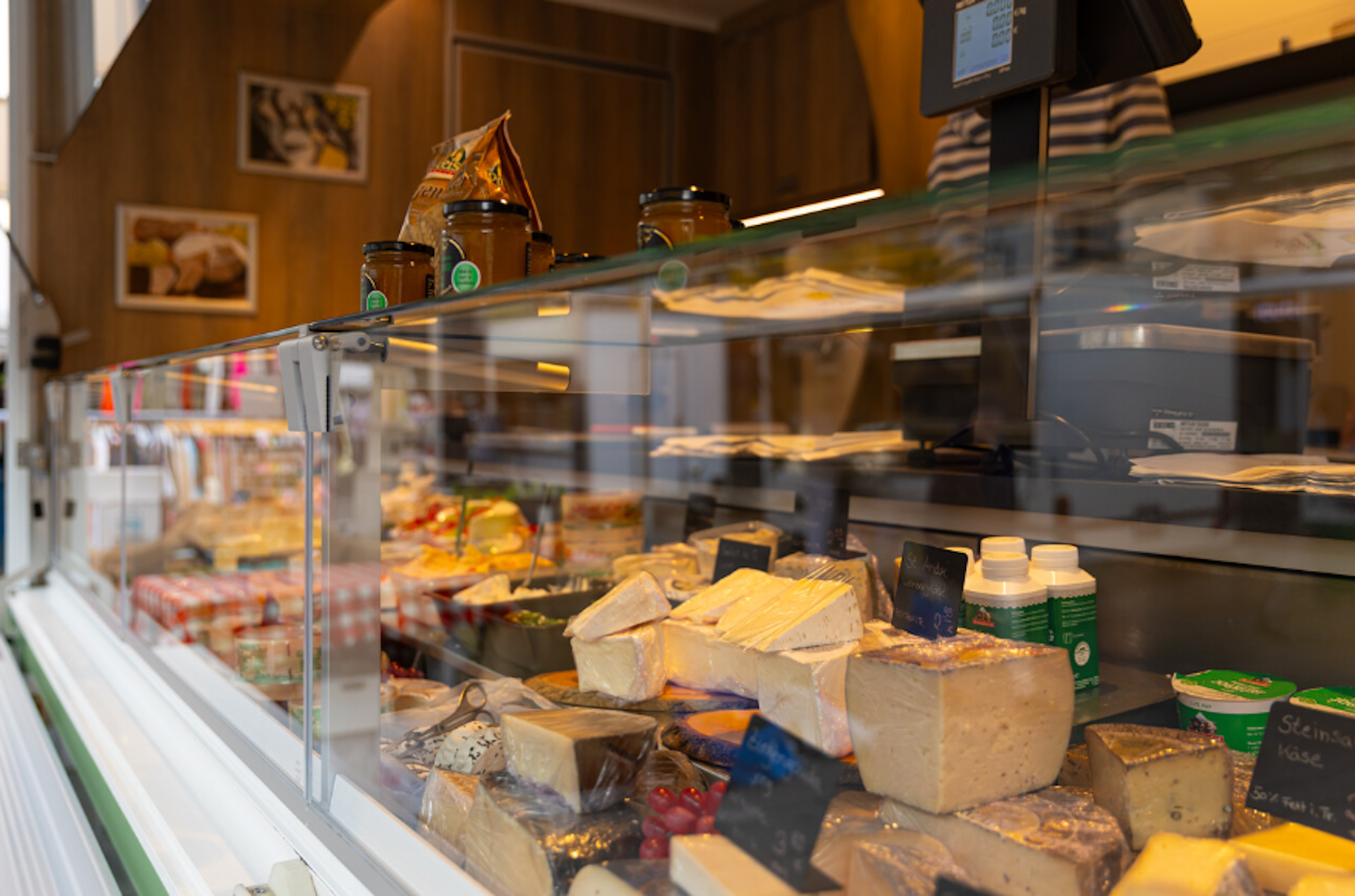 Das Foto zeigt eine gut gefüllte Käsetheke auf einem Marktstand. Verschiedene Käsesorten sind sorgfältig präsentiert und mit kleinen Tafeln beschriftet.