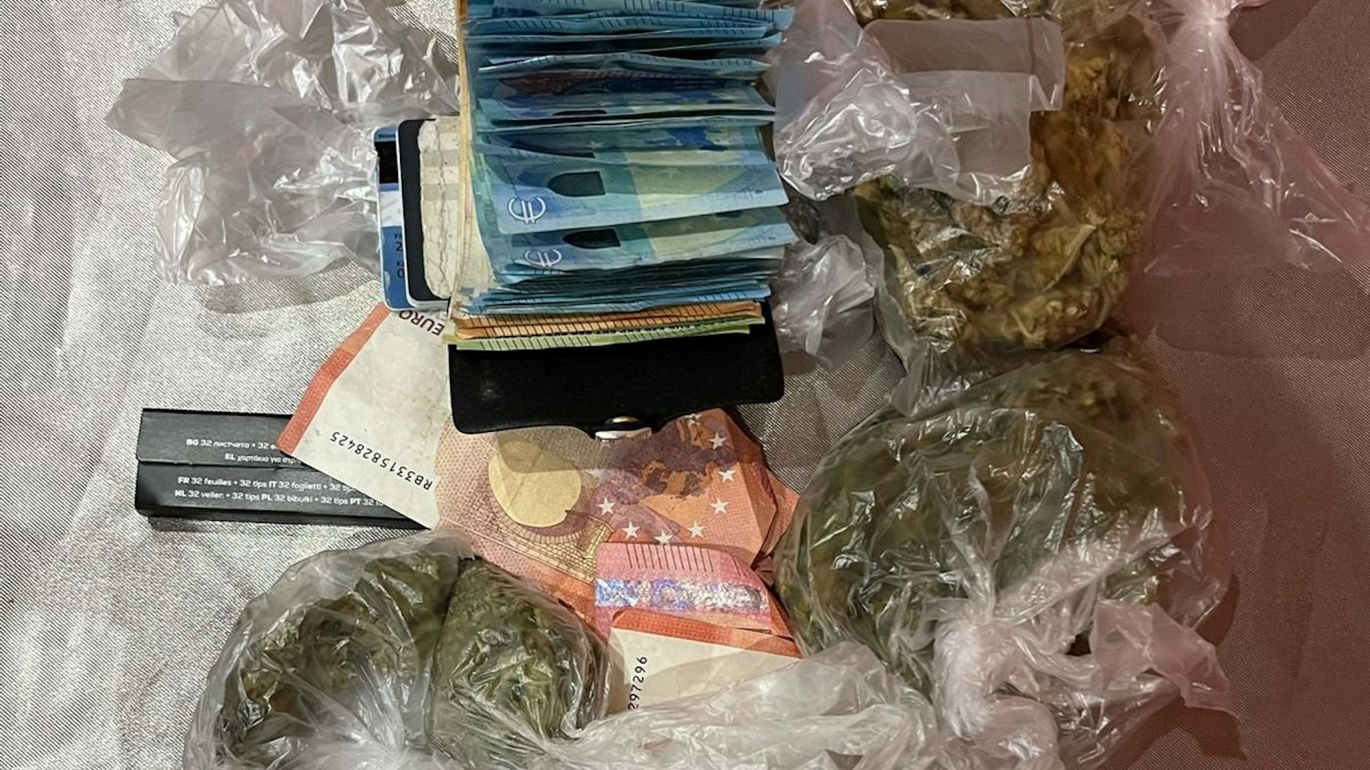 Beschlagnahmtes Drogengeld und verschiedene Drogenpäckchen liegen auf einem Tisch.