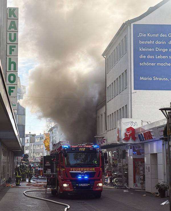 Einsatzkräfte stehen in einer Einkaufstraße vor einem Geschäft, aus dem dichter Rauch quillt. Ein Feuer in einem Laden der Einkaufsmeile Hochstraße hat einen Großeinsatz der Feuerwehr in der Innenstadt ausgelöst.