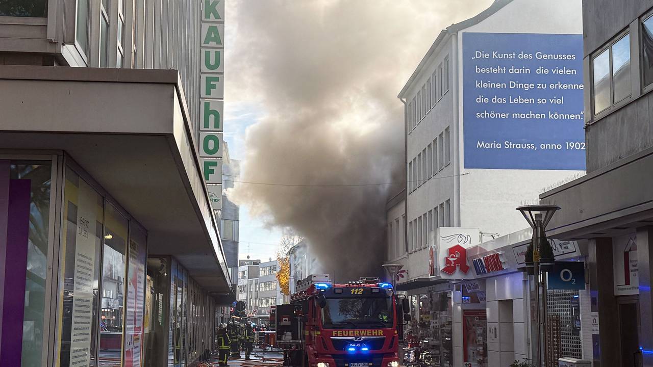 Einsatzkräfte stehen in einer Einkaufstraße vor einem Geschäft, aus dem dichter Rauch quillt. Ein Feuer in einem Laden der Einkaufsmeile Hochstraße hat einen Großeinsatz der Feuerwehr in der Innenstadt ausgelöst.